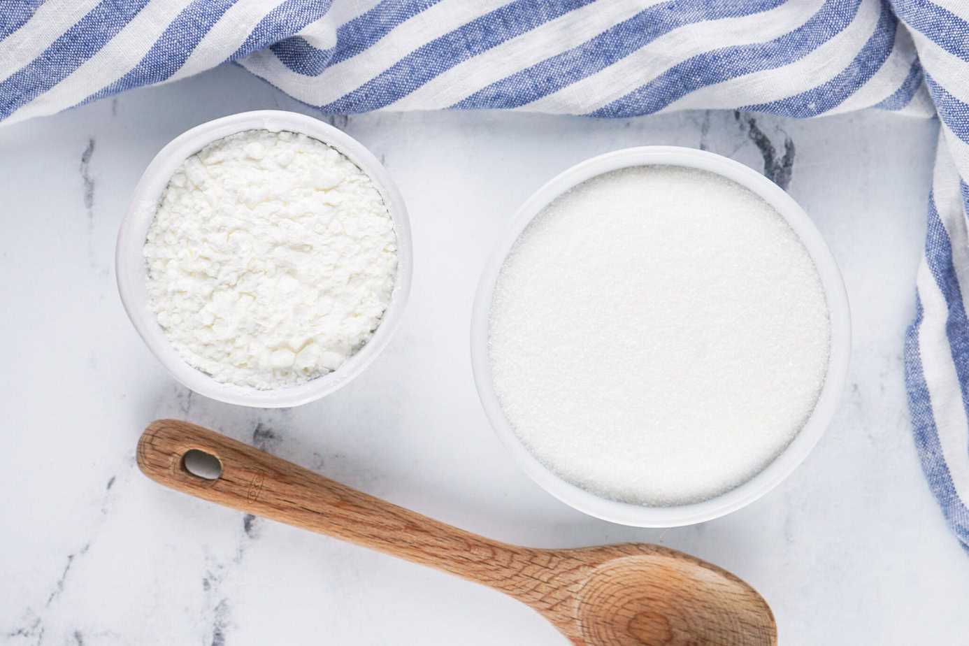 corn starch and granulated sugar - homemade powdered sugar ingredients in small white bowls with a wooden spoon next to them
