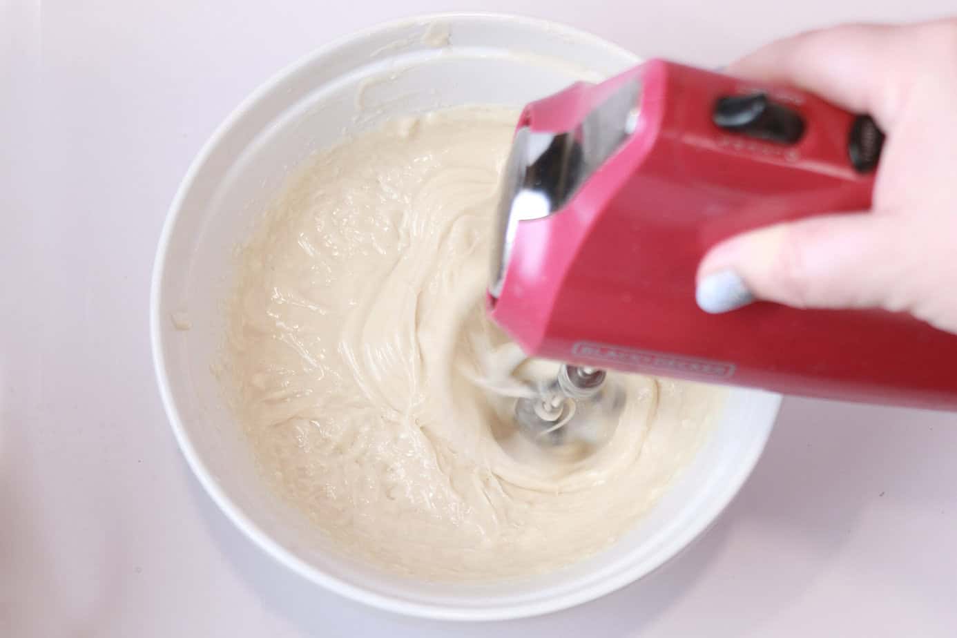 using an electric mixer to mix up cake goop ingredients in a white bowl