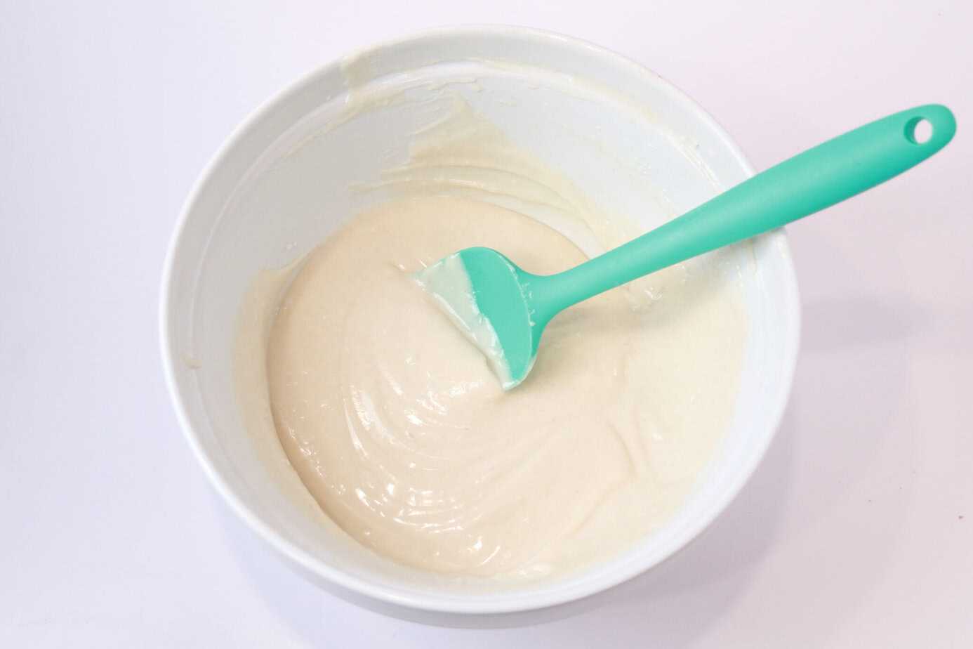 cake goop in a white bowl with a silicone spoon