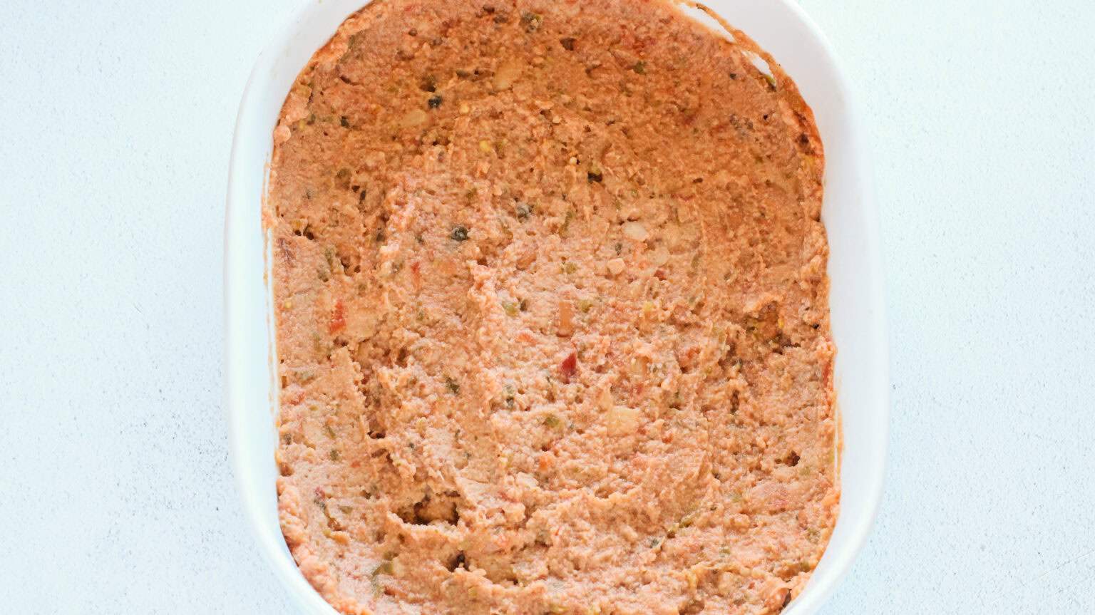 white oval baking dish with beans and salsa mix spread in bottom