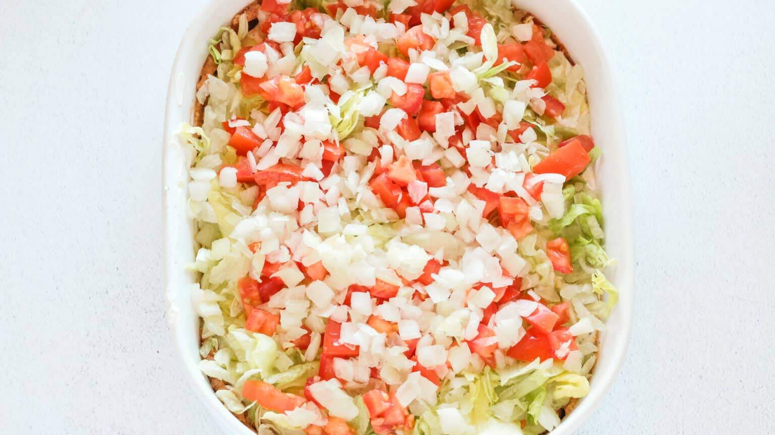 lettuce tomato and onion layer in a white baking dish