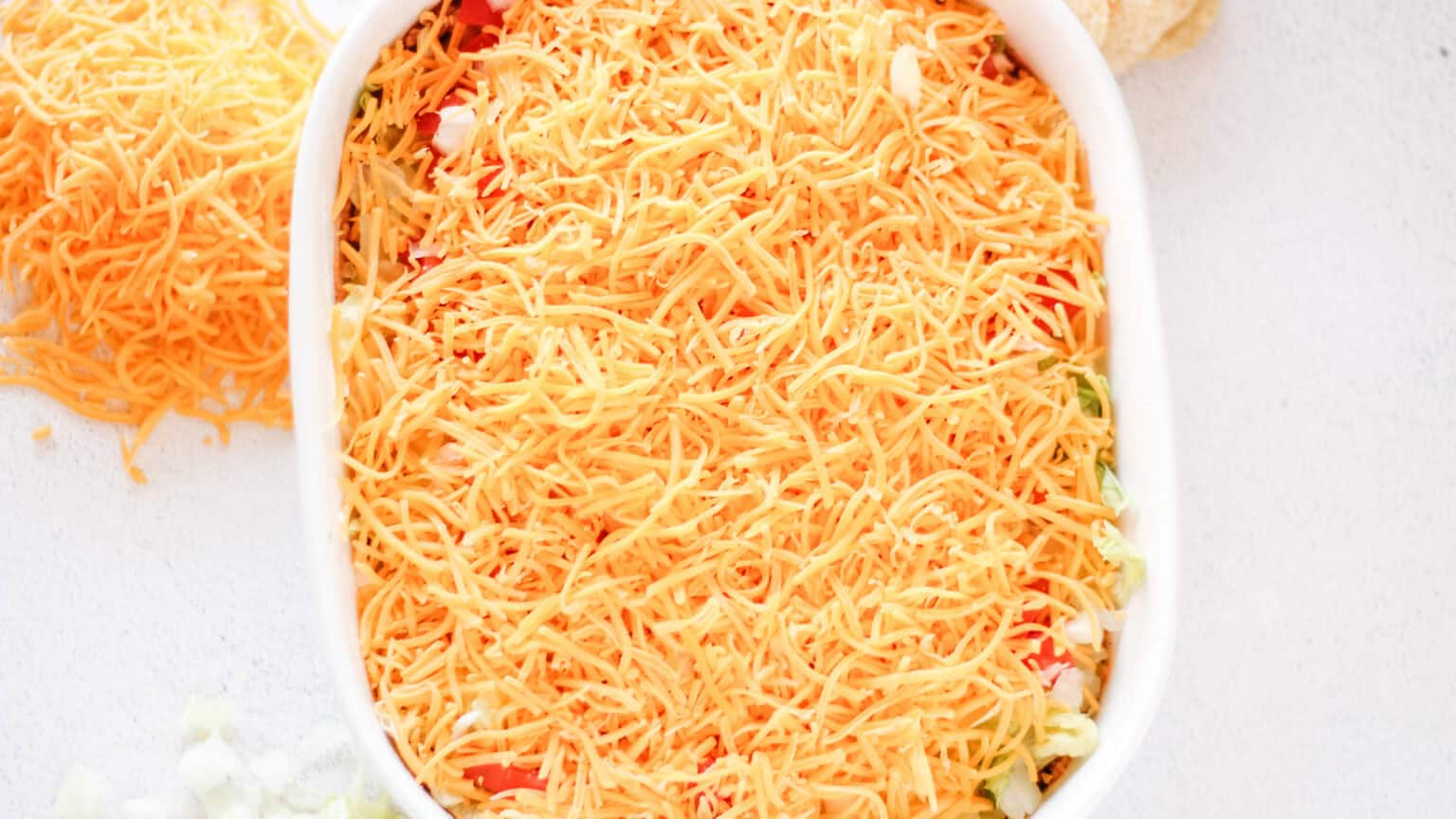 lettuce tomato and onion layer in a white baking dish with cheese on top