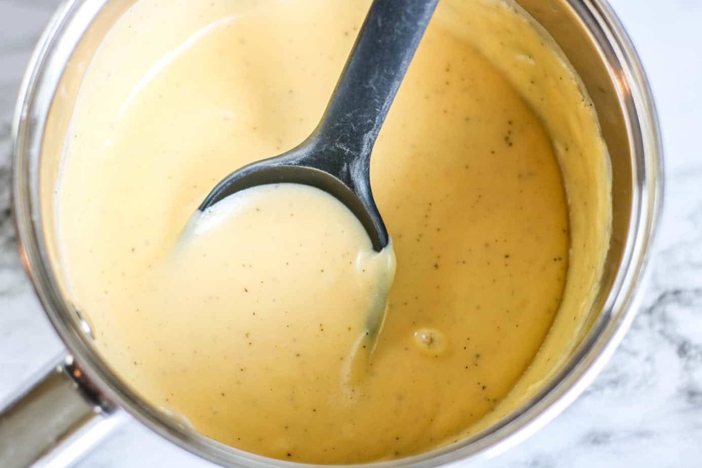 Cheese sauce in a small saucepan with a black spoon