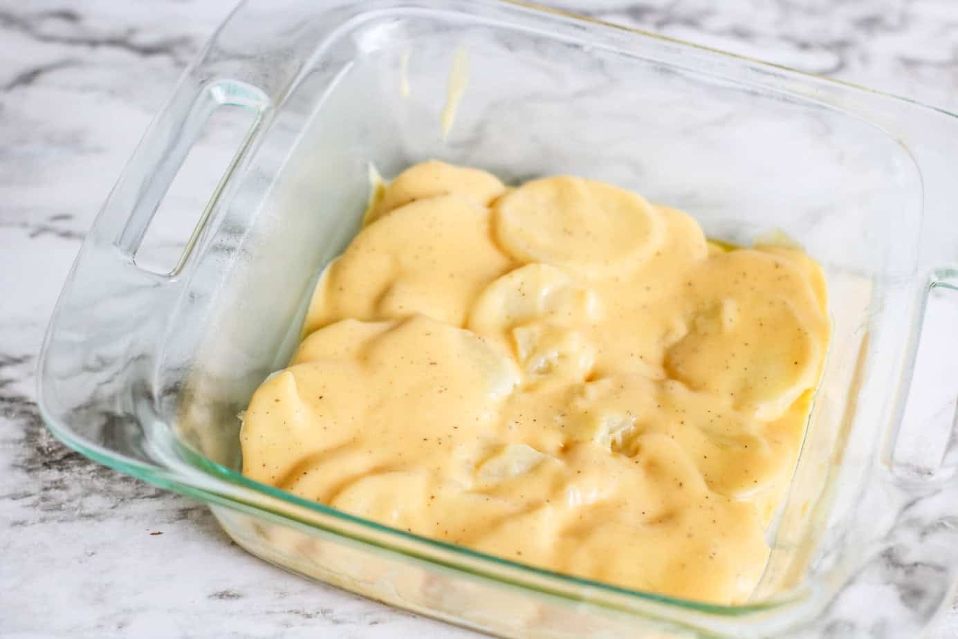 sliced potatoes with cheesy sauce in a clear square baking dish