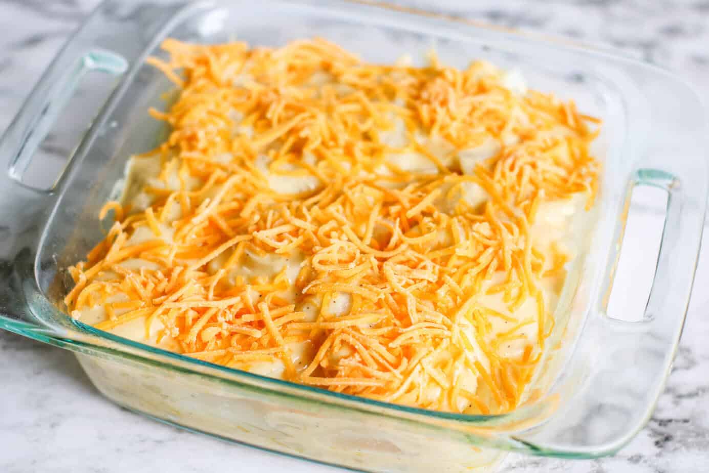 shredded cheese over sliced potatoes with cheese sauce in a clear baking dish