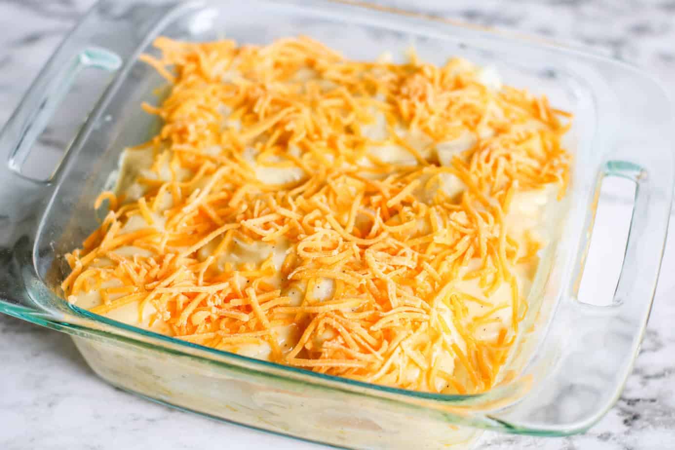 shredded cheese over sliced potatoes with cheese sauce in a clear baking dish