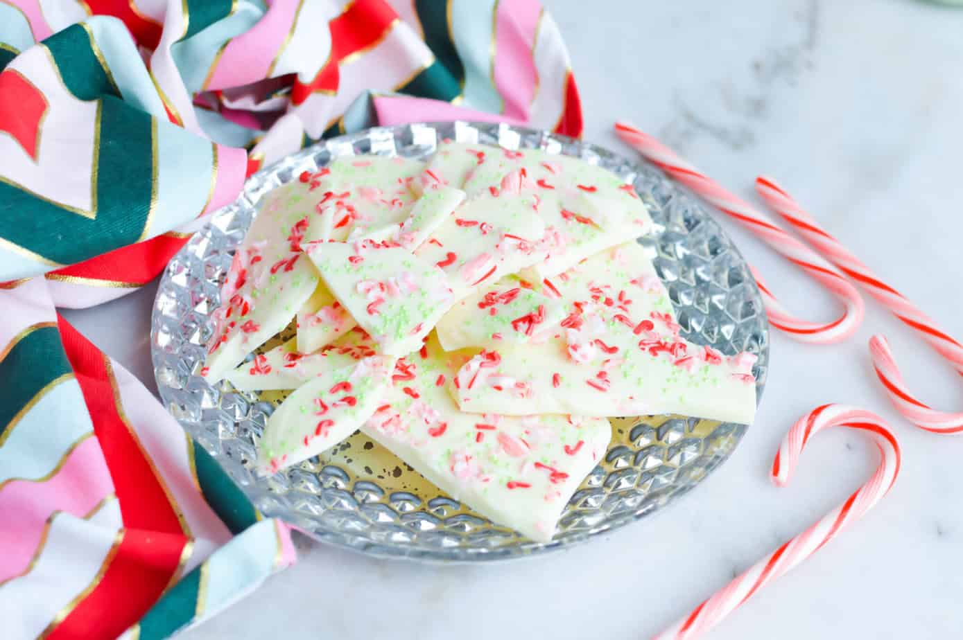 white chocolate peppermint bark on a silver cookie plate with candy canes and christmas fabric around it