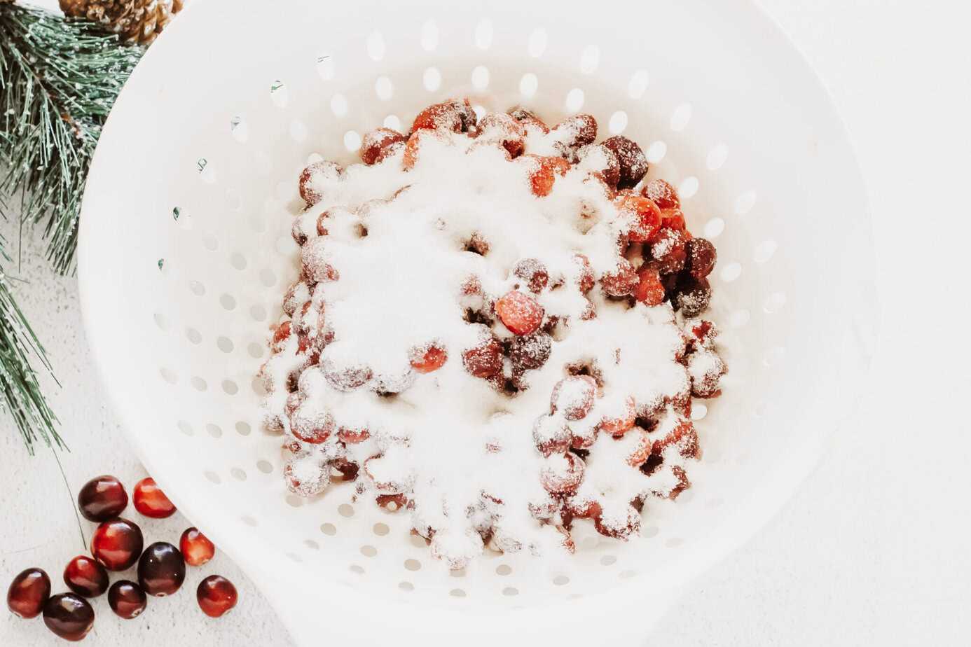 syrup coated cranberries in a strainer with sugar poured on top
