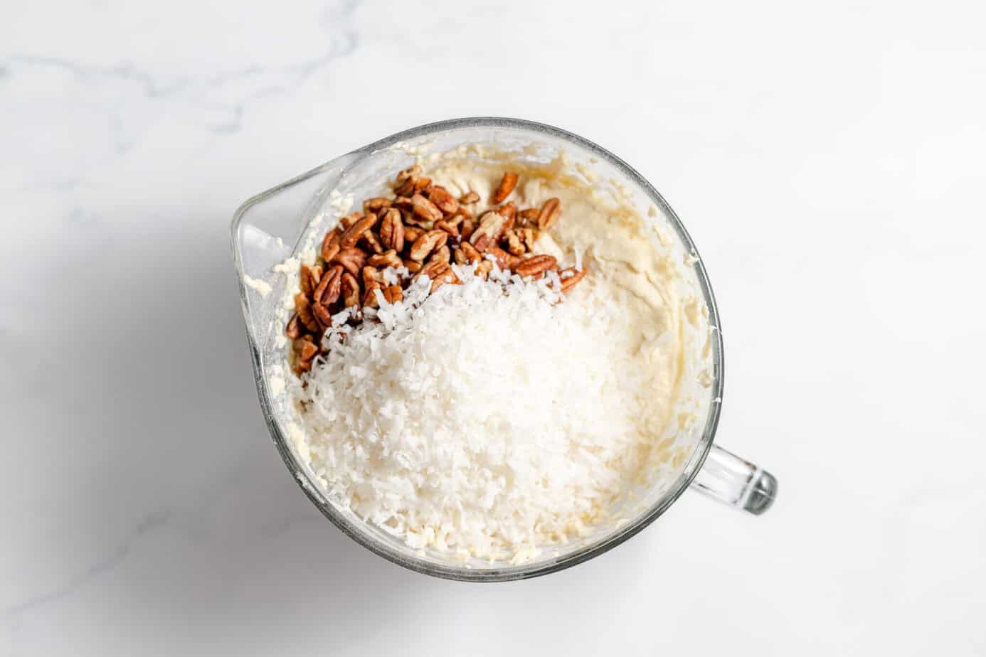 coconut and pecans added to mixed cake batter in clear bowl