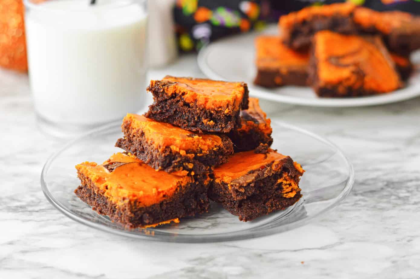 halloween brownies on a clear plate with a glass of milk next to it and halloween decorations