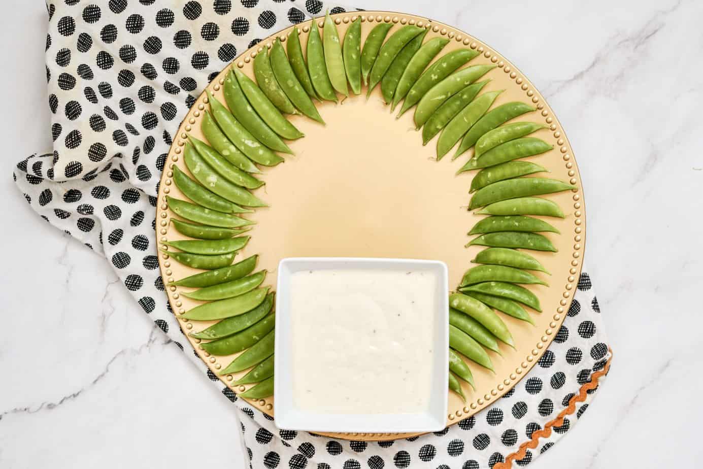 sugar snap peas around the outside of a platter with a bowl of dip at the bottom