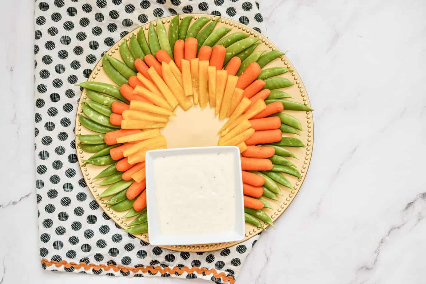 Yellow bell pepper sticks and carrots inside the sugar snap peas around the outside of a platter 