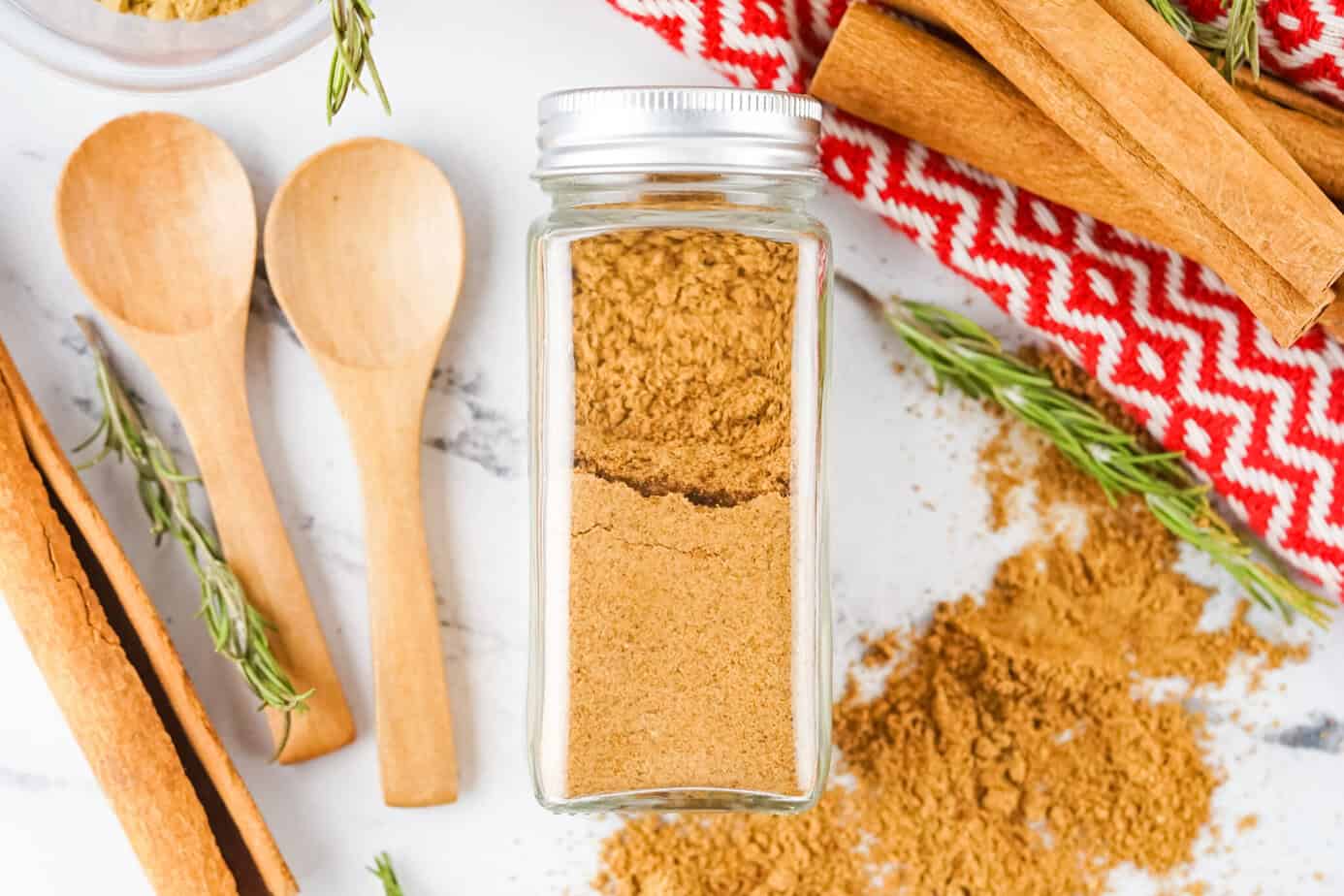 homemade gingerbread spice in a jar spilled on a surface with spoons and cinnamon sticks