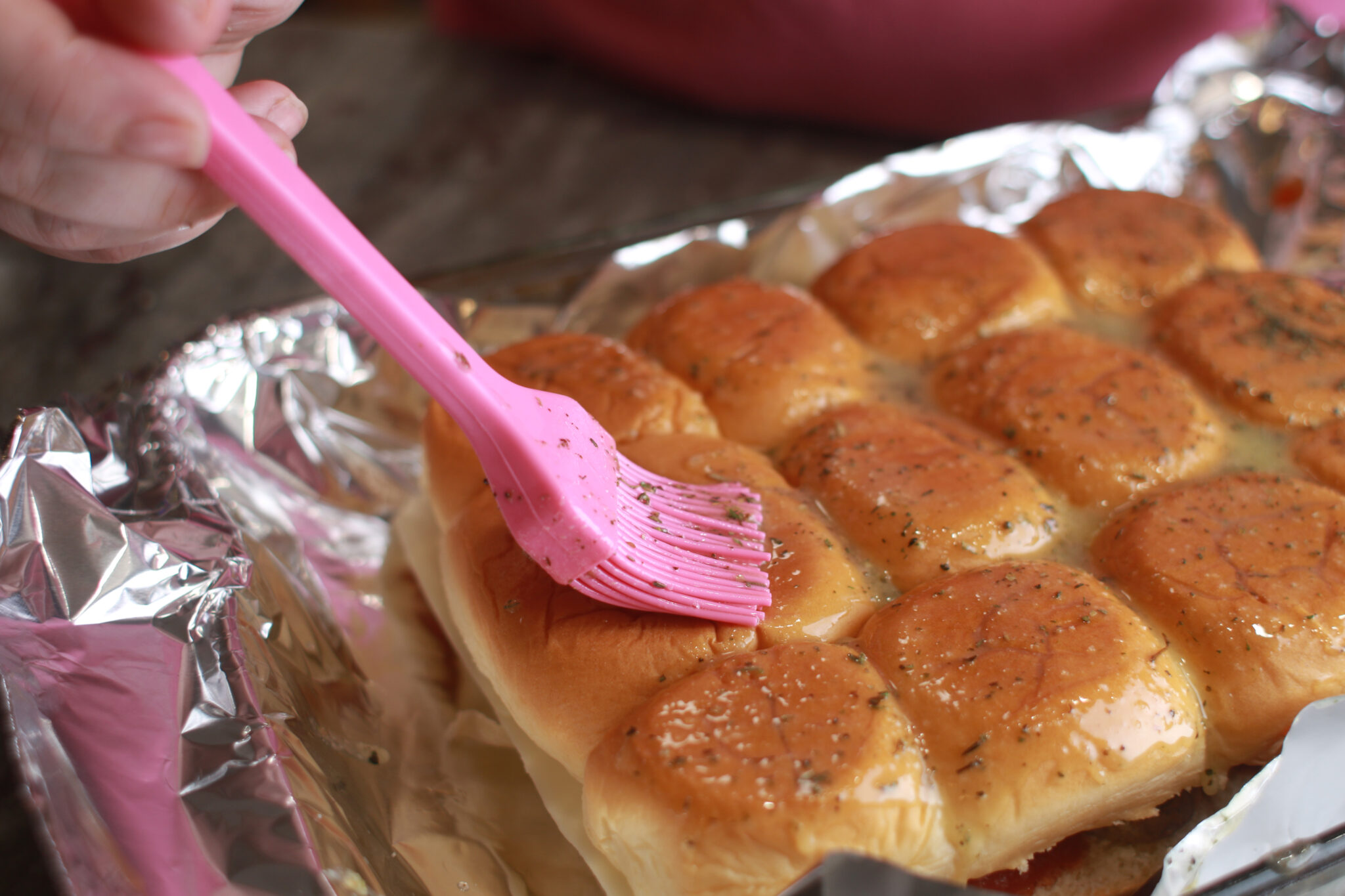 brushing garlic butter onto hawaiian rolls for meatball sliders