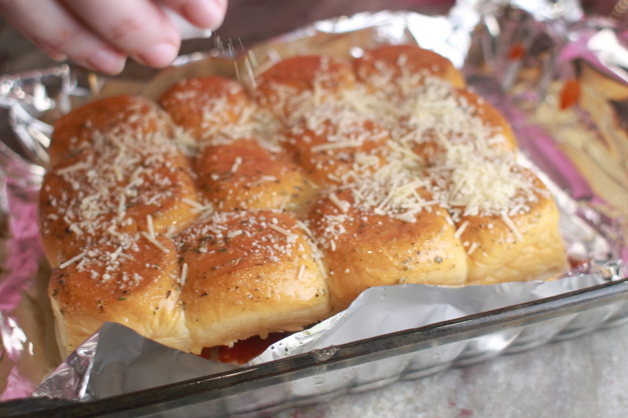sprinkling parmesan on hawaiian roll meatball sliders