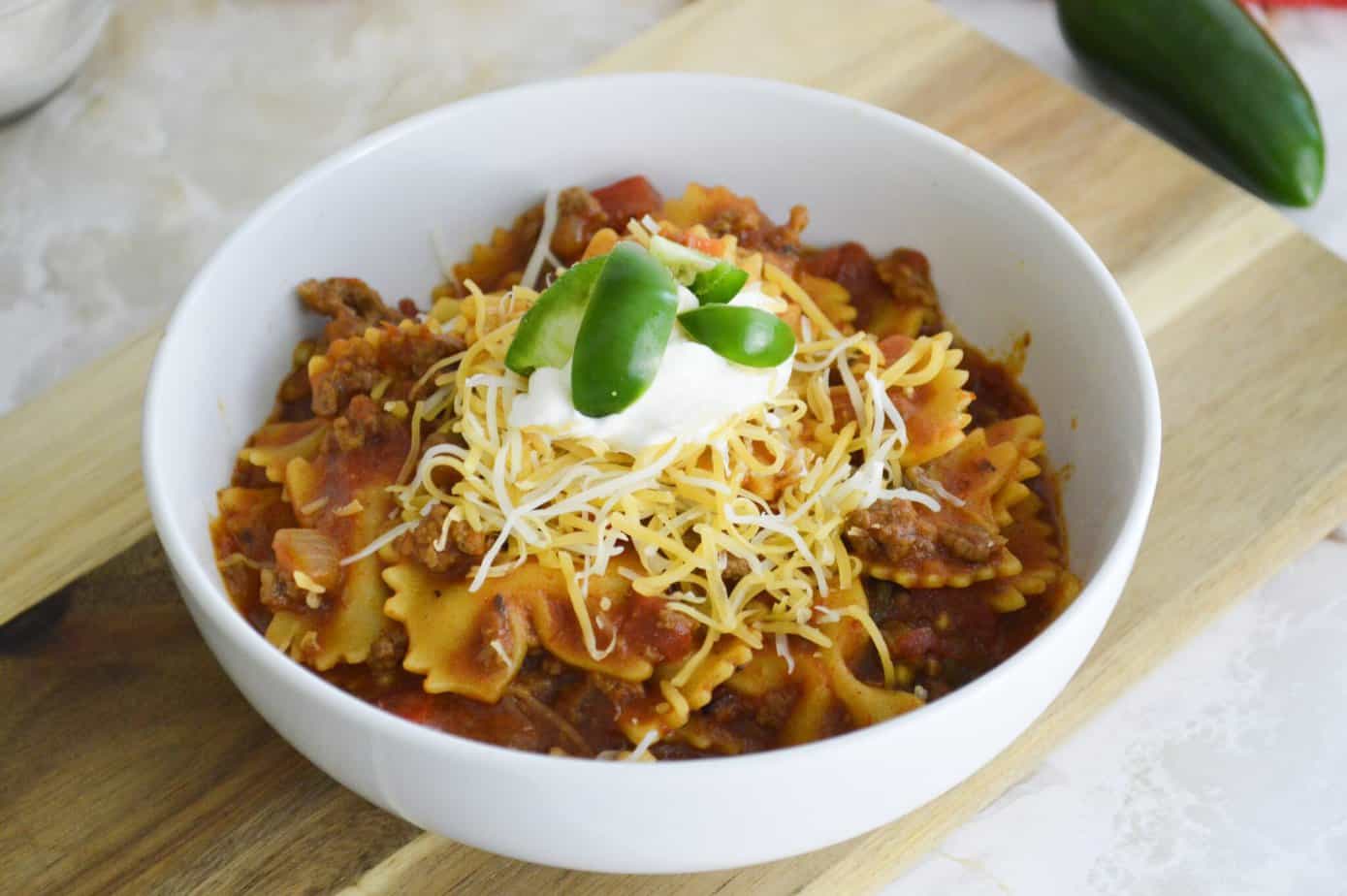 Instant Pot taco Pasta in a white bowl with sour cream, cheese and fresh jalapeno on top