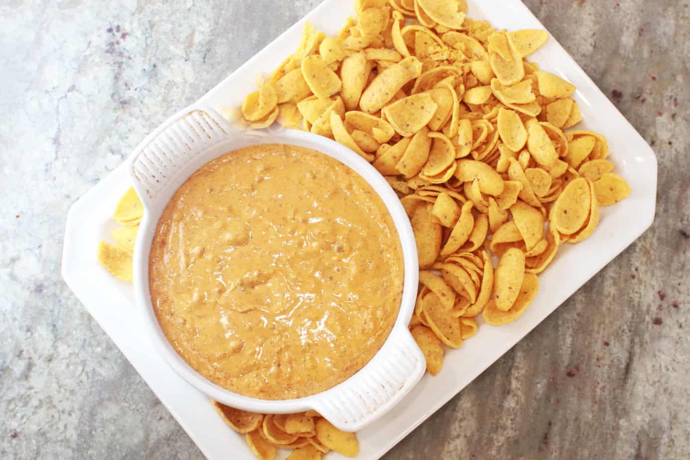 hormel chili cheese dip in a round white baking dish with fritos scoops on a white platter