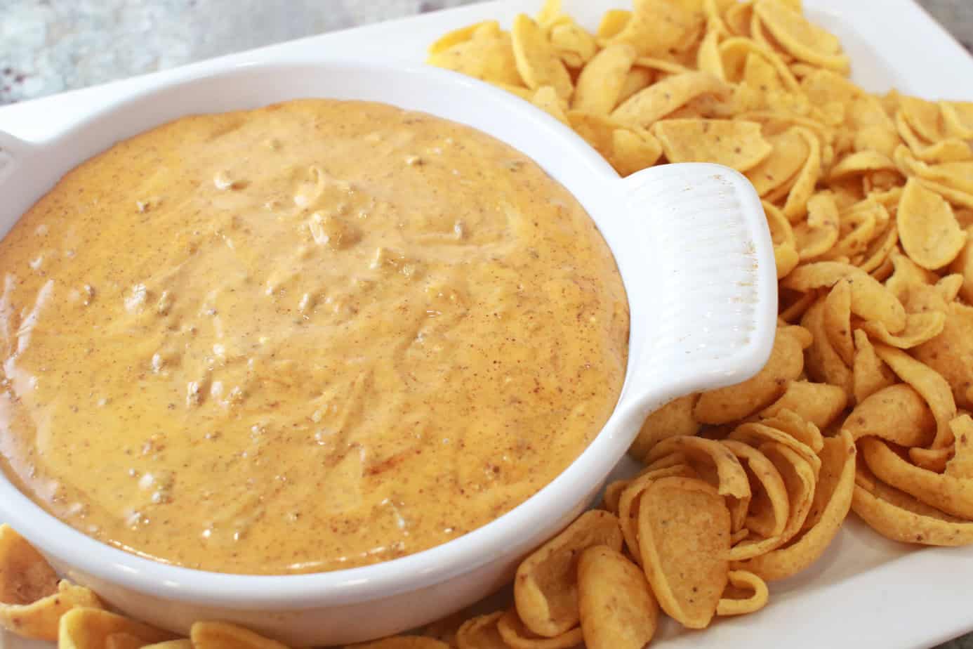 Velveeta chili cheese dip in a round white baking dish with fritos scoops on a white platter