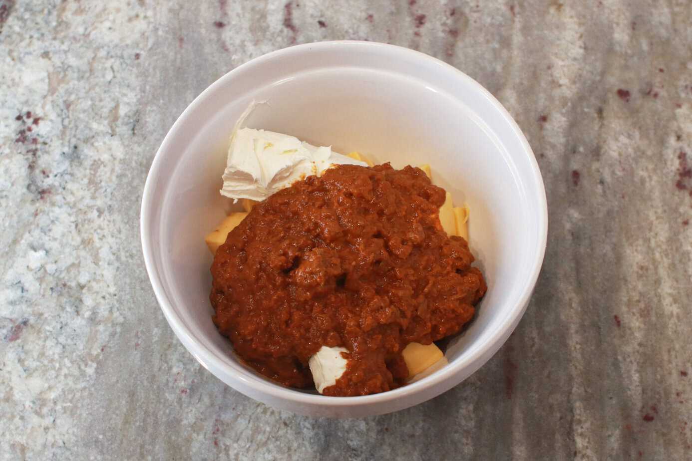 hormel chili poured over cubed velveeta and cream cheese in white mixing bowl