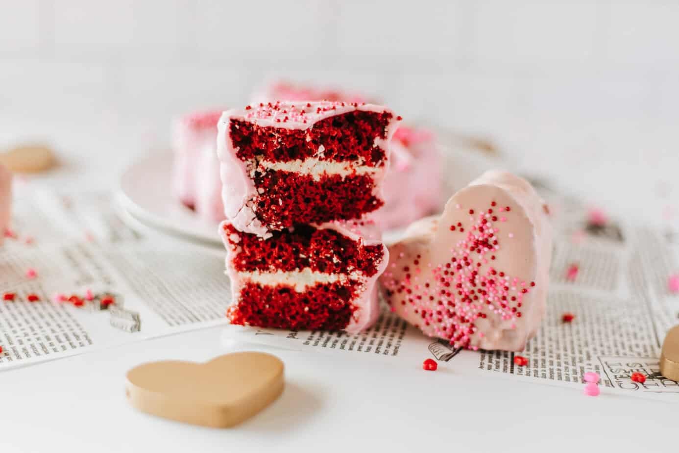 A cake cut in half to show the red velvet cake and filling next to a pink chocolate dipped one