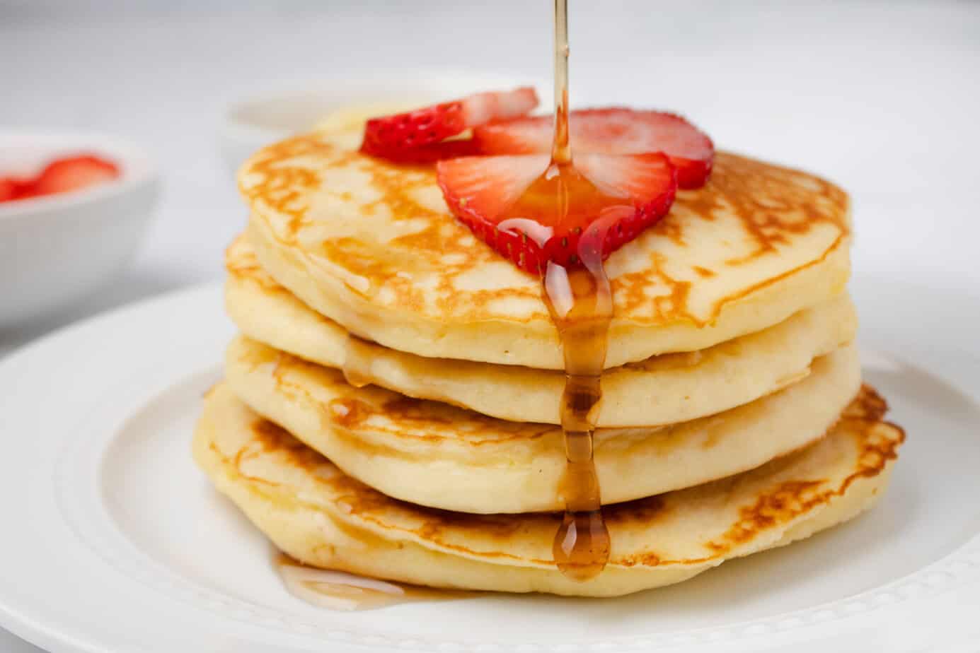 lemon ricotta pancakes with strawberries on top and maple syrup drizzling