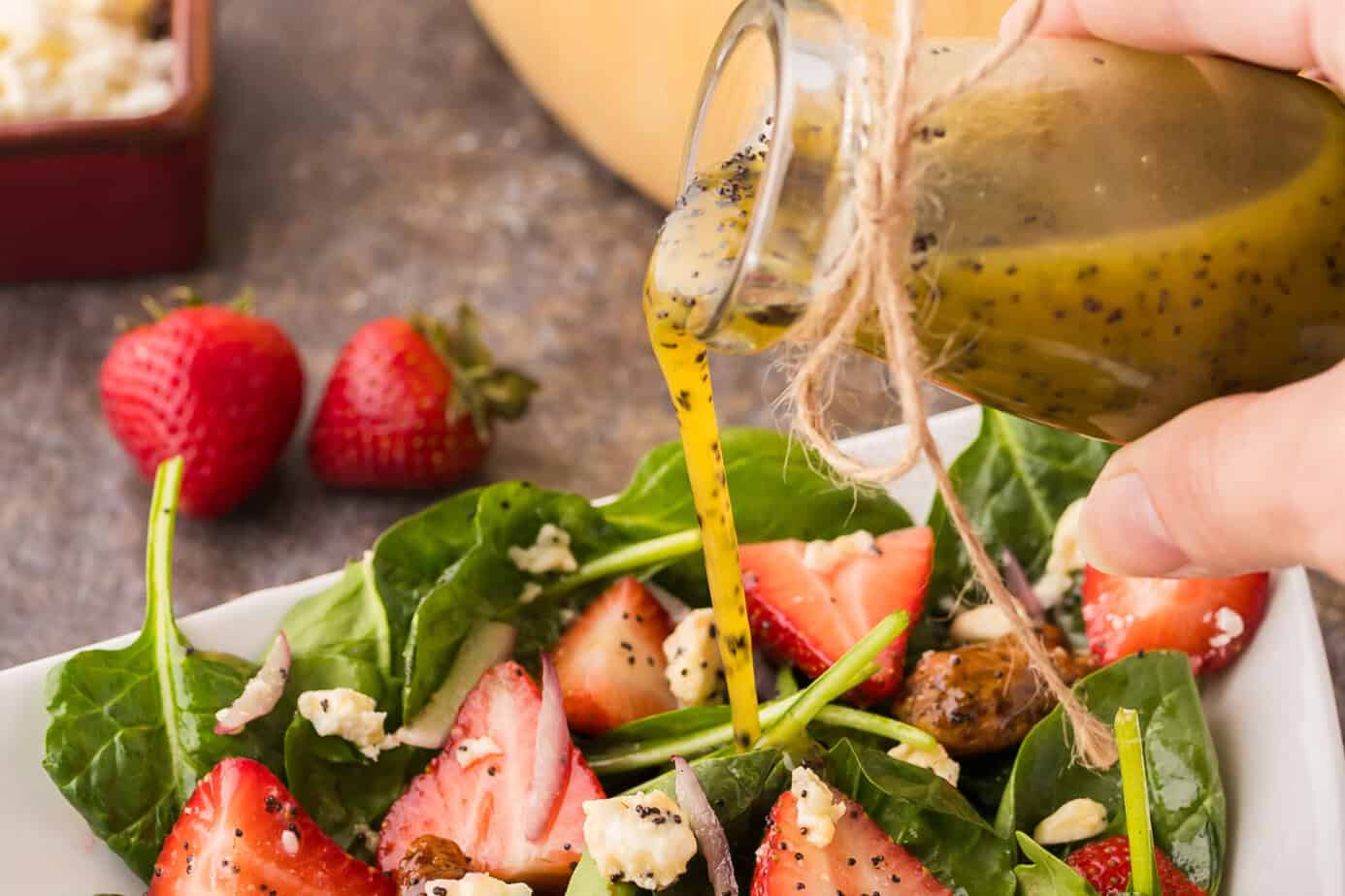 pouring poppy seed dressing onto a strawbery spinach salad