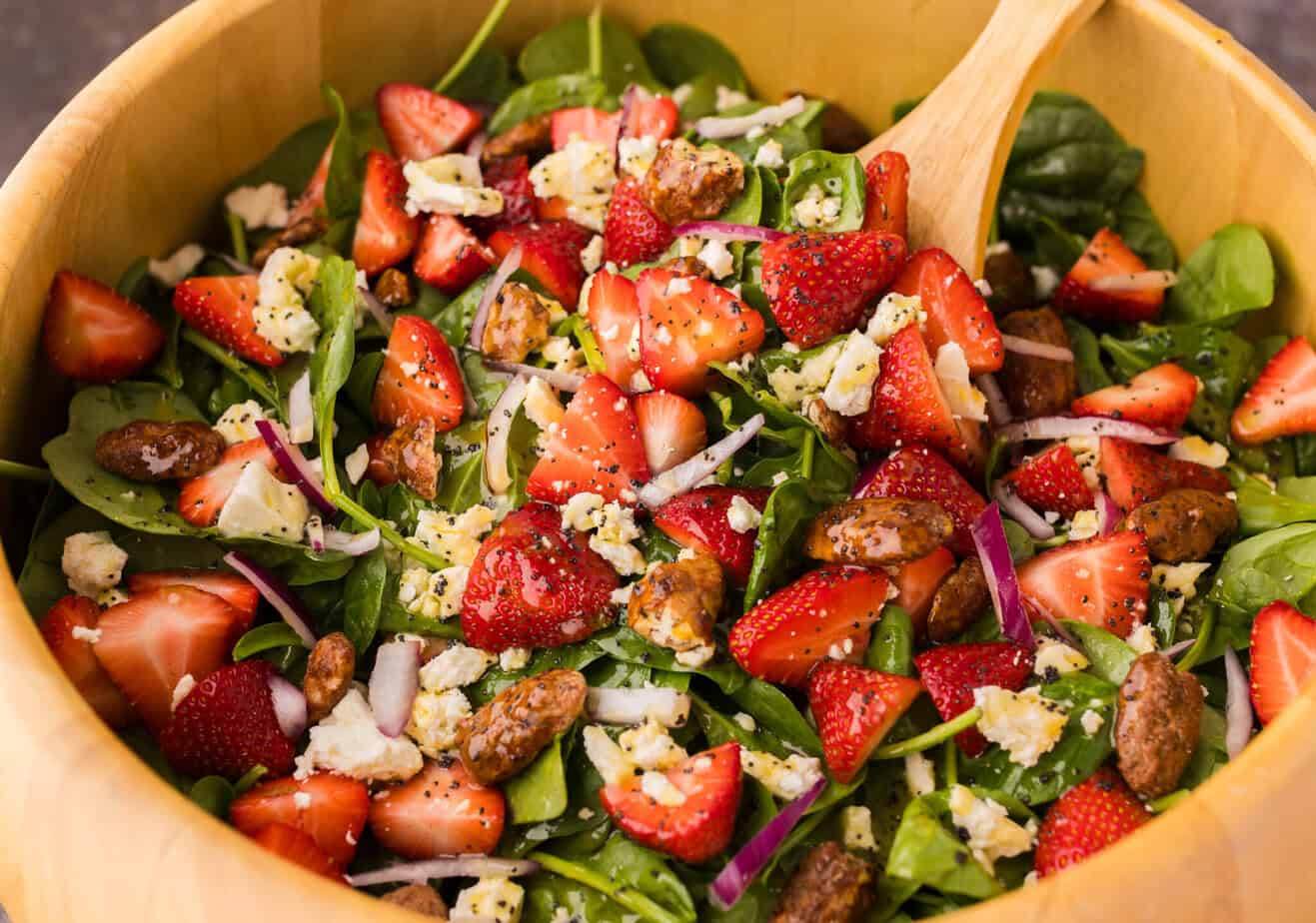 Strawberry Feta Spinach Salad in a wooden bowl with a wooden spoon on a gray surface