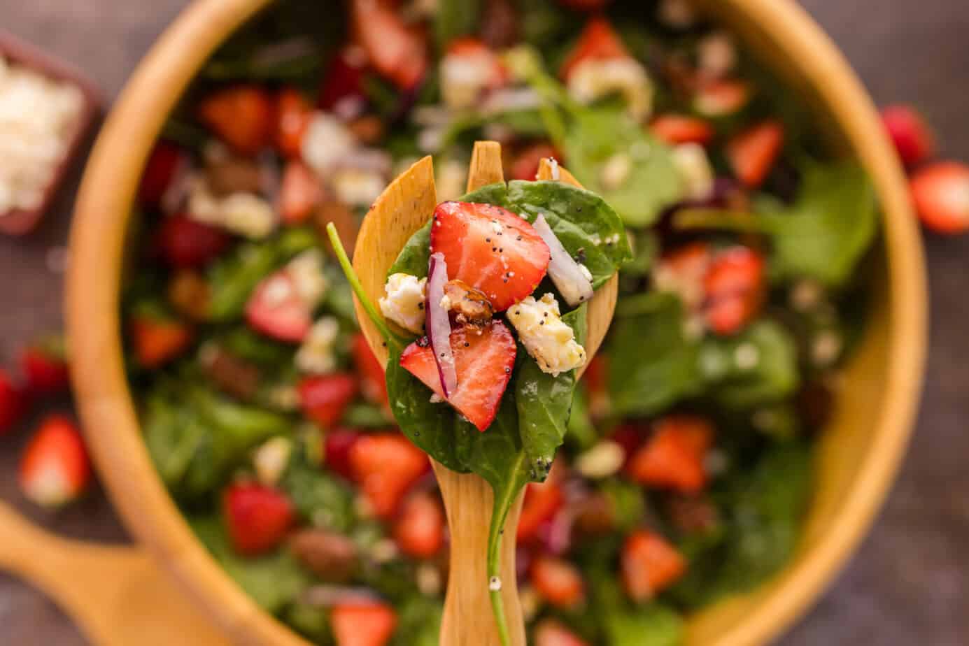 Strawberry Spinach Feta Salad in a wooden bowl with a wooden spoon