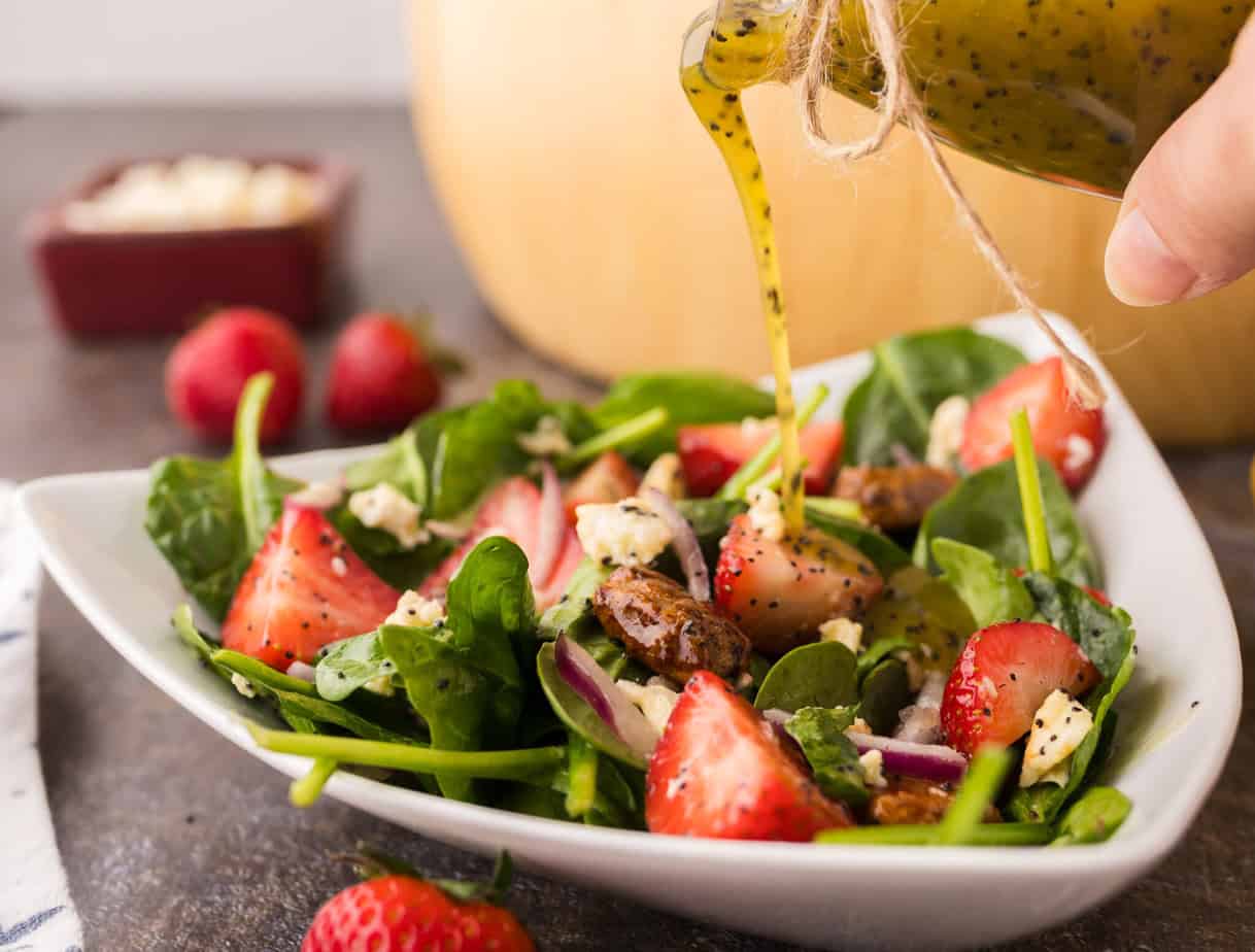 pouring poppyseed salad dressing on spinach strawberry salad