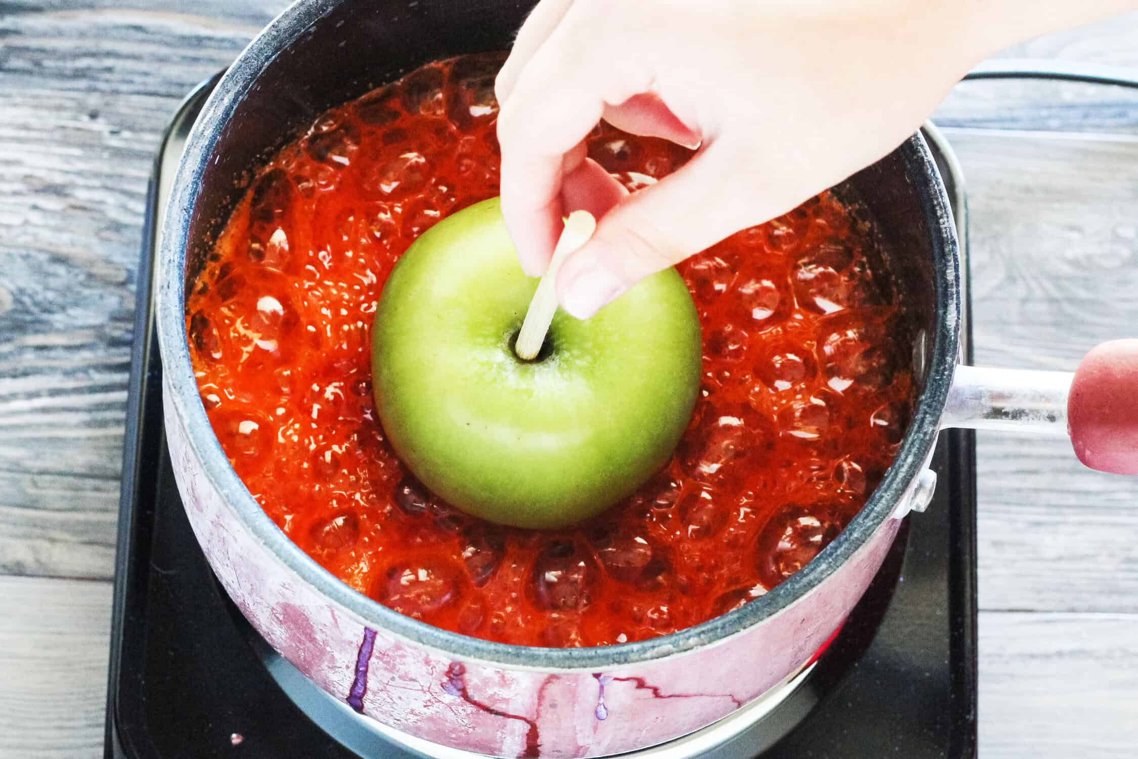 dipping an apple in colored sugar that is boiling