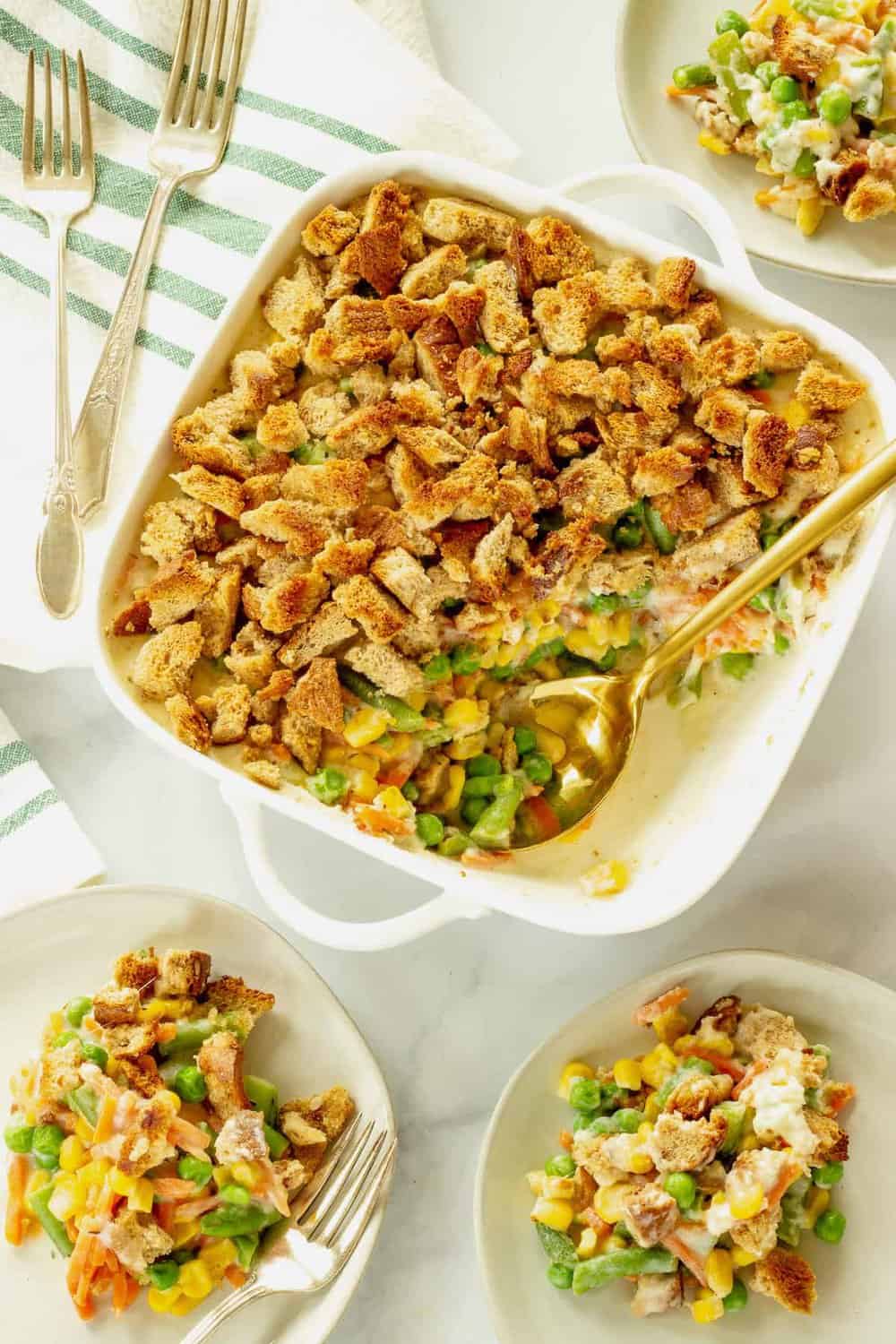 Mixed vegetable casserole in a square baking dish with a gold serving spoon.