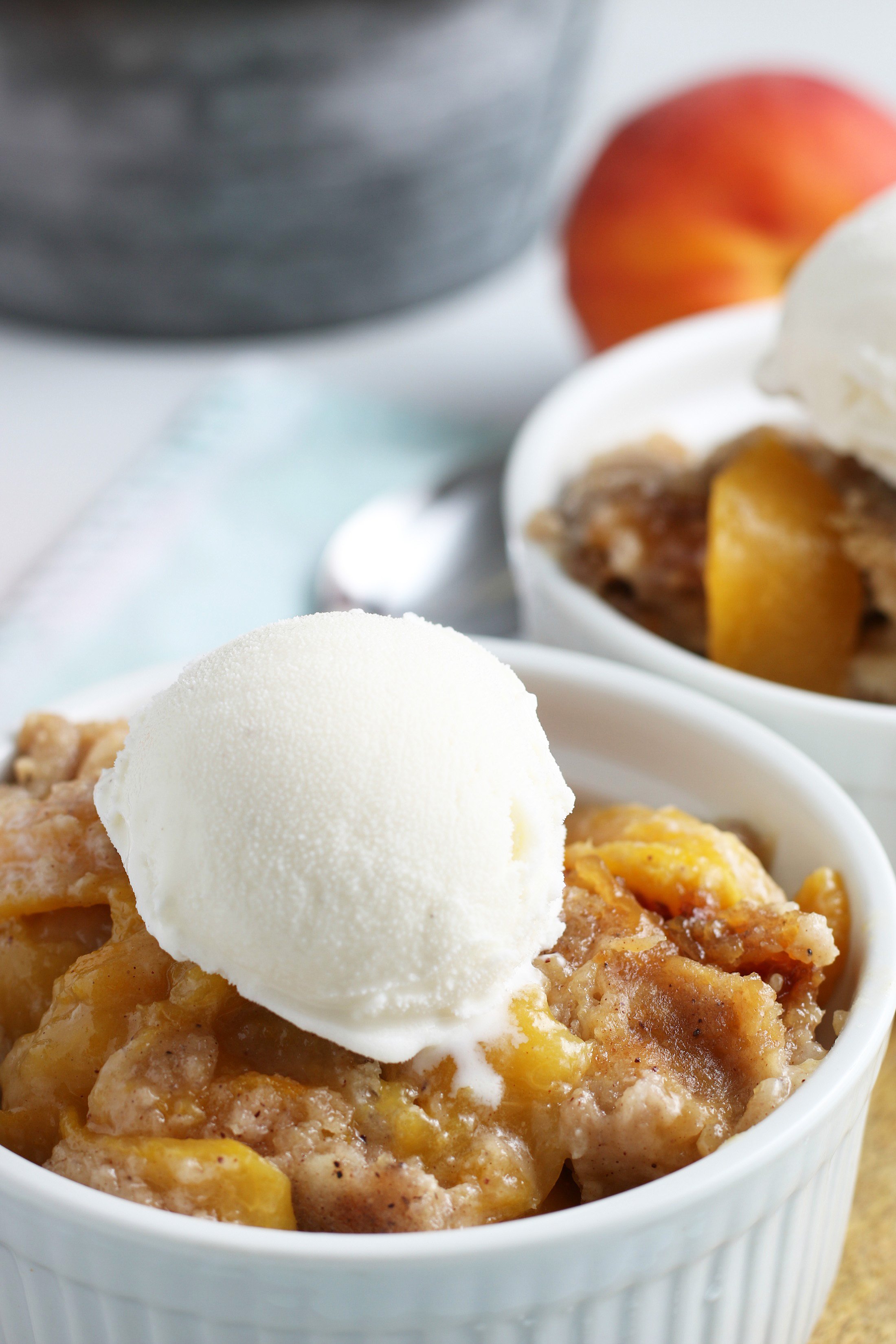 crockpot peach cobbler in a white bowl with a scoop of vanilla ice cream on top