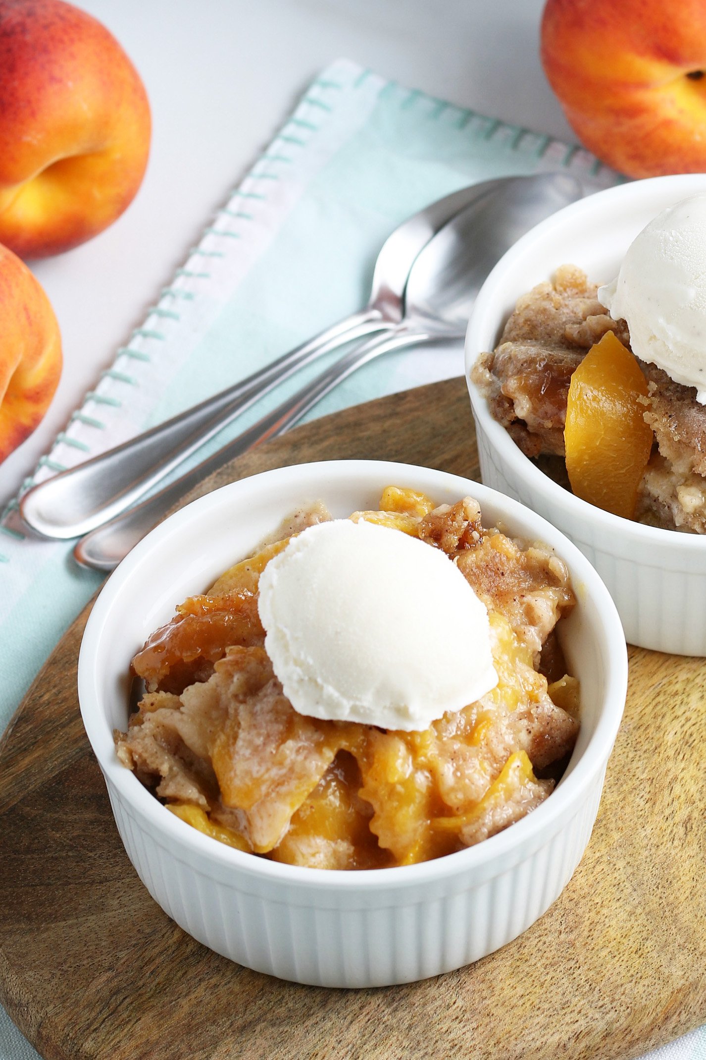 crockpot peach cobbler individual serving in a white bowl with a scoop of vanilla ice cream