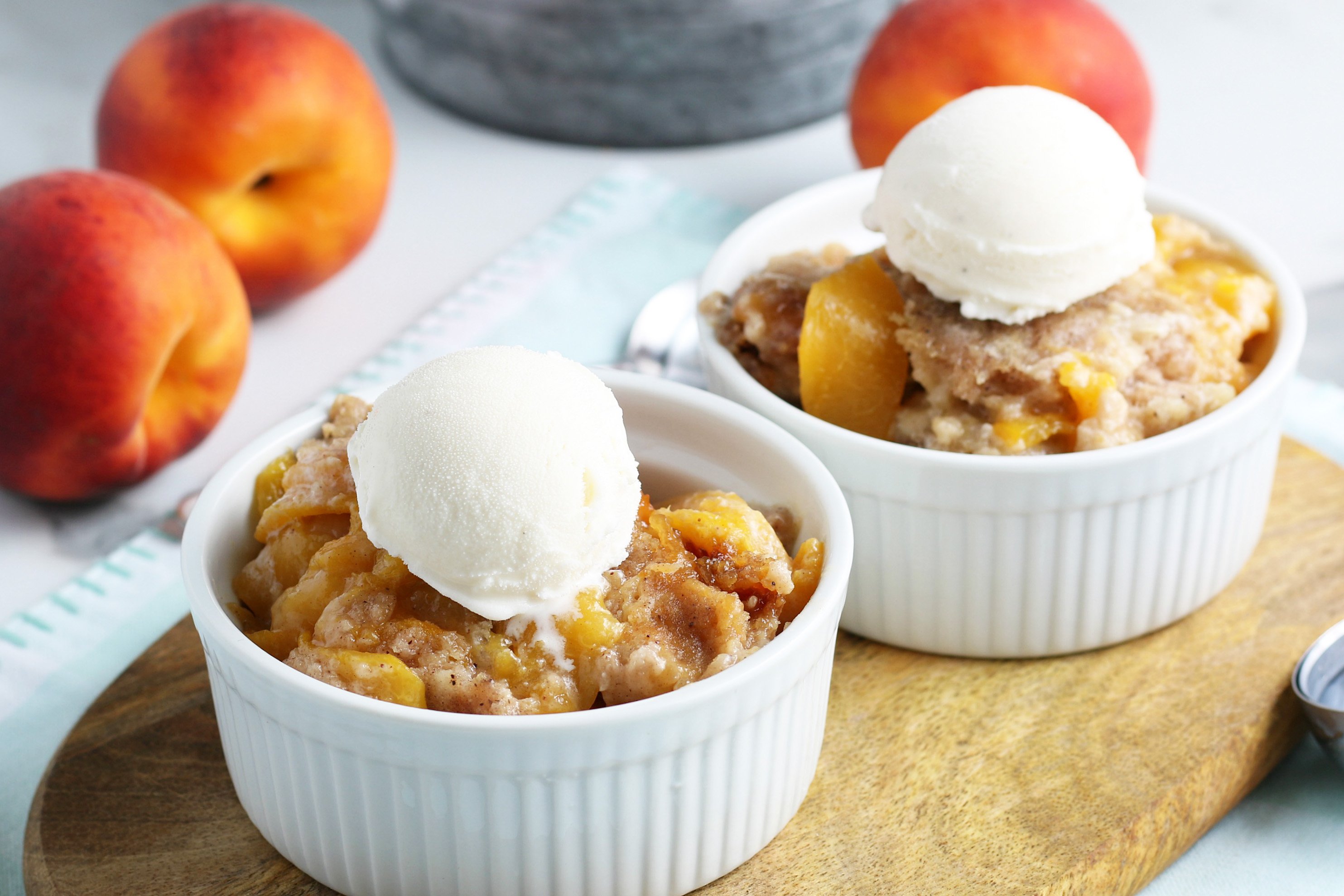 crockpot peach cobbler individual serving in a white bowl with a scoop of vanilla ice cream