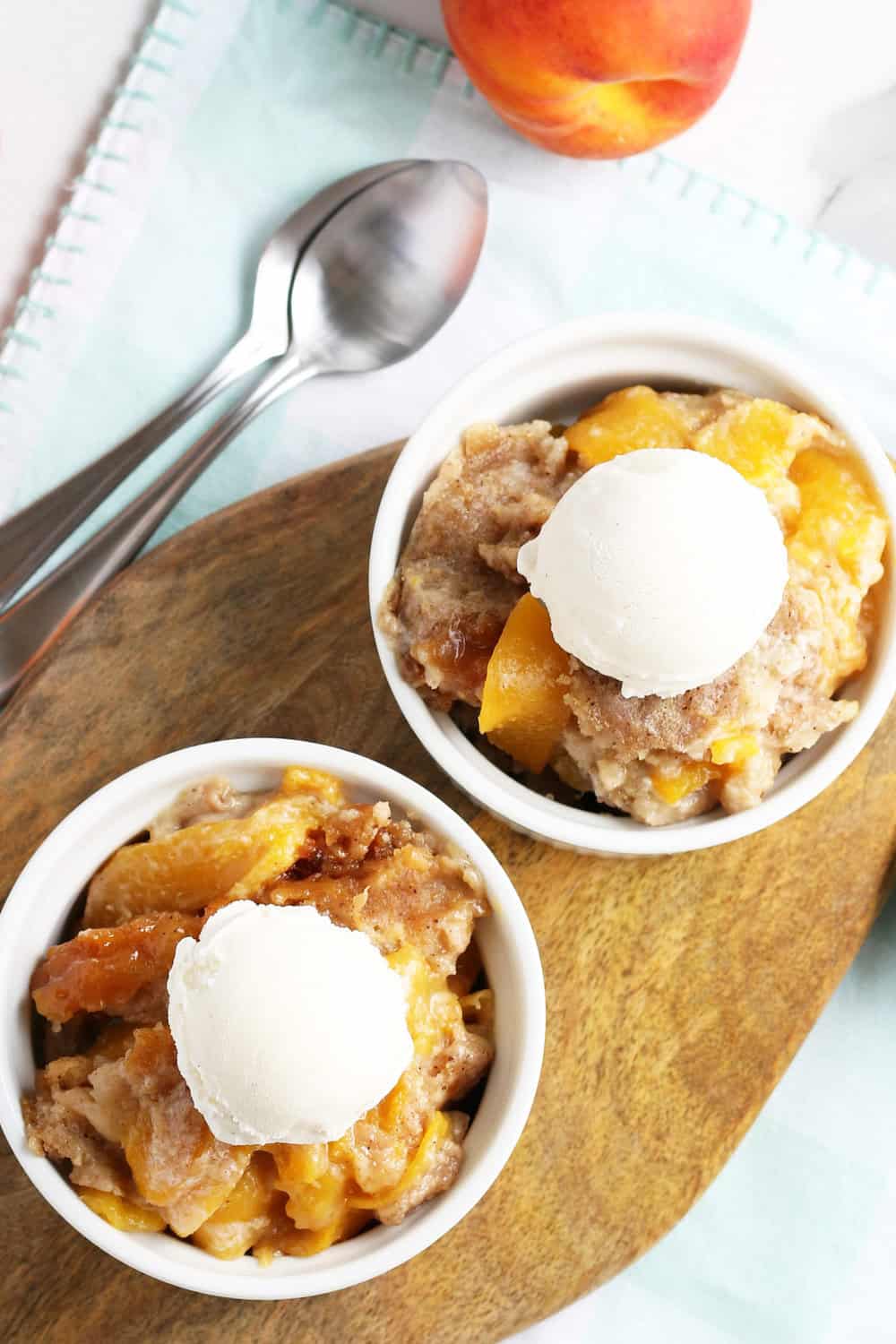 crockpot peach cobbler individual serving in a white bowl with a scoop of vanilla ice cream