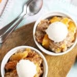 crockpot peach cobbler in individual serving bowls with a scoop of vanilla ice cream