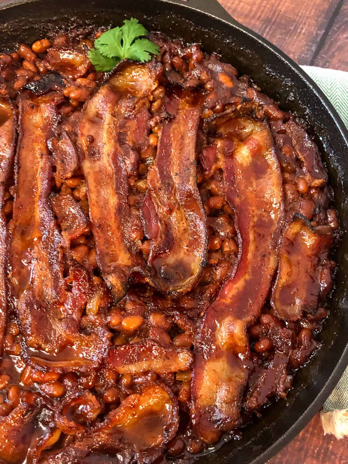 Iron skillet of baked beans with strips of crispy bacon on top.