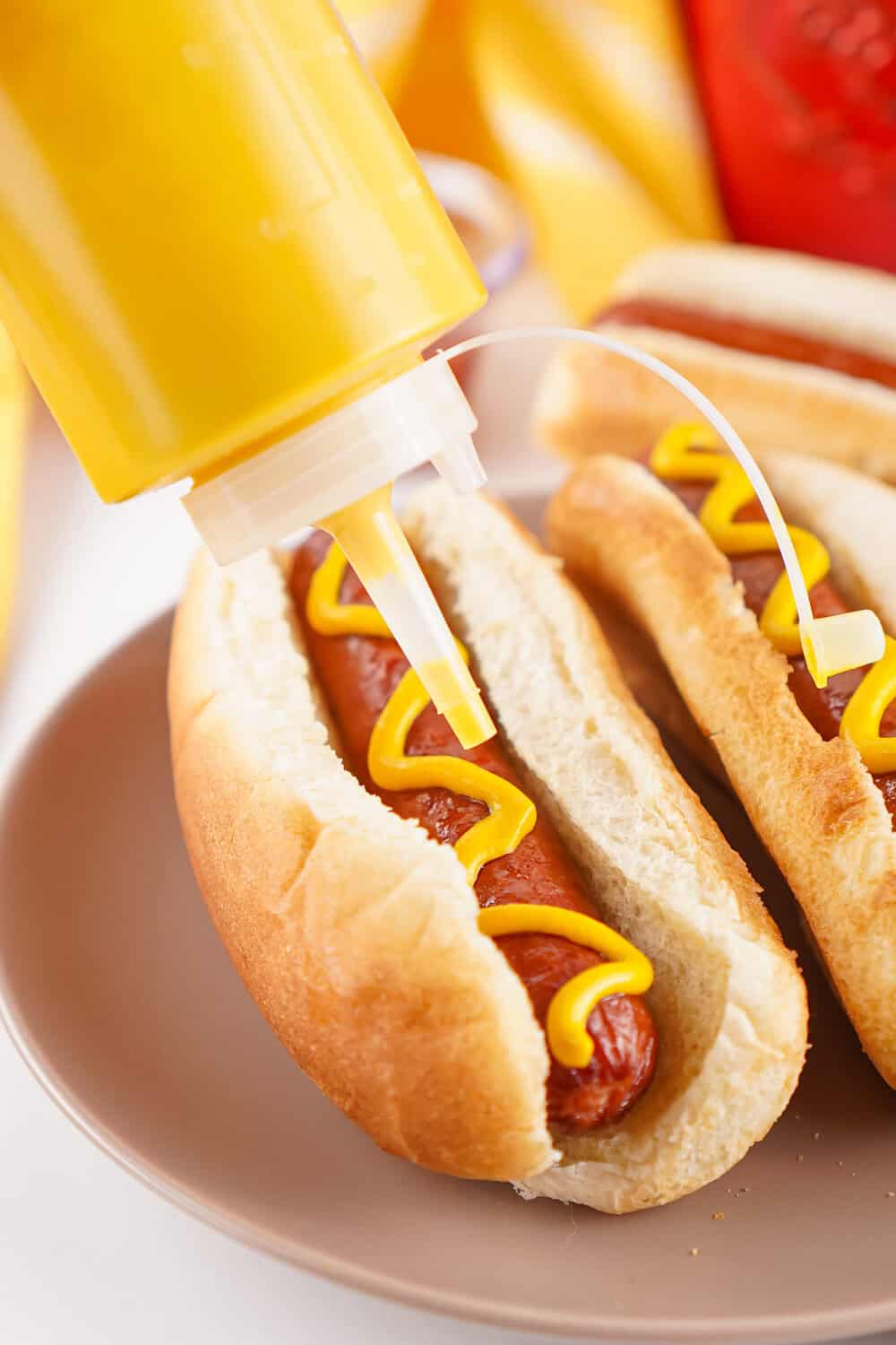 mustard being squirt onto a hot dog in a bun