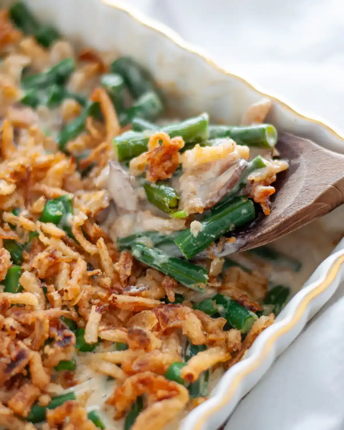 Homemade green bean casserole lifting out of the dish with a wooden spoon.