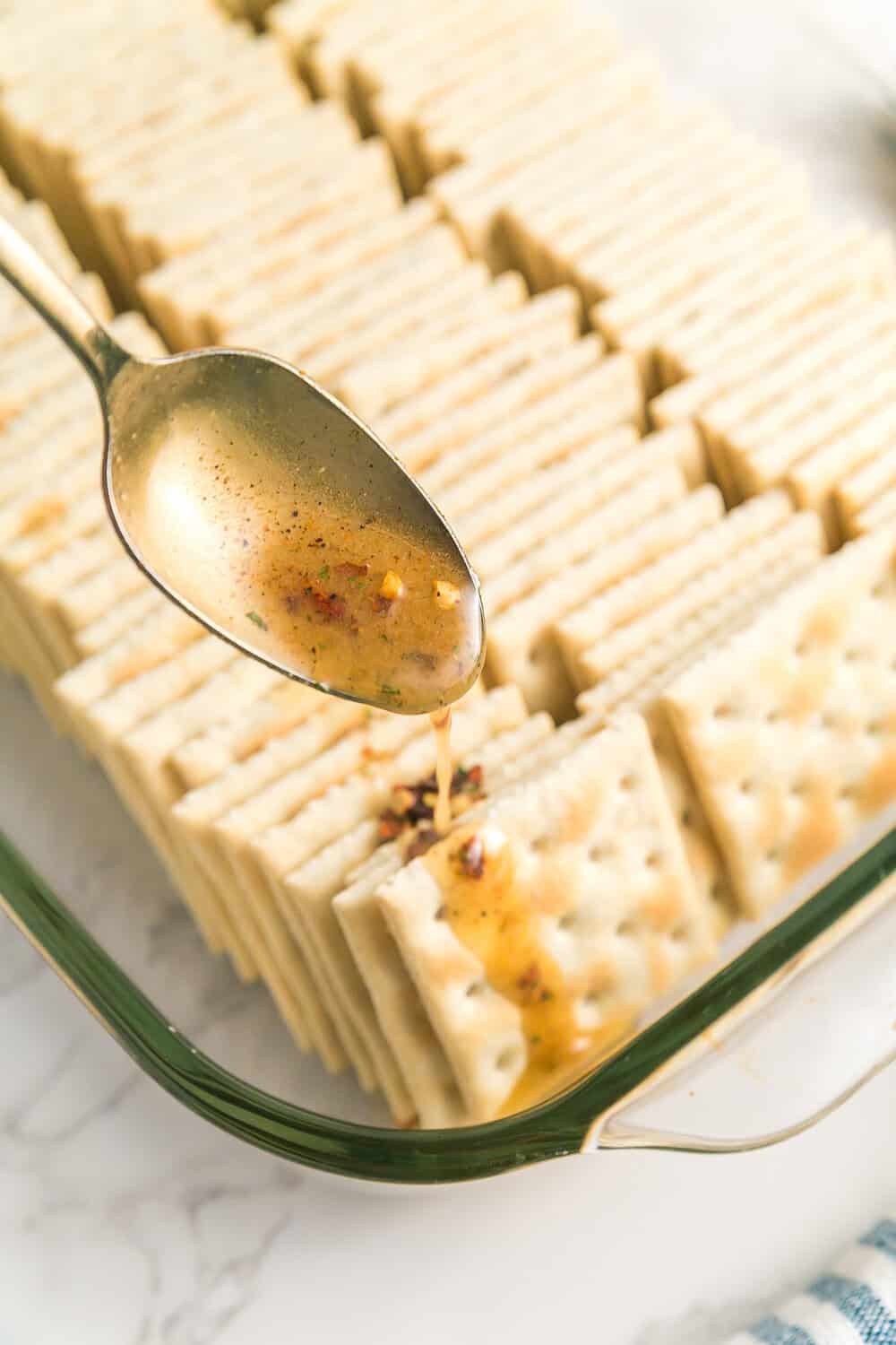 spooning seasoning mix over rows of saltine crackers
