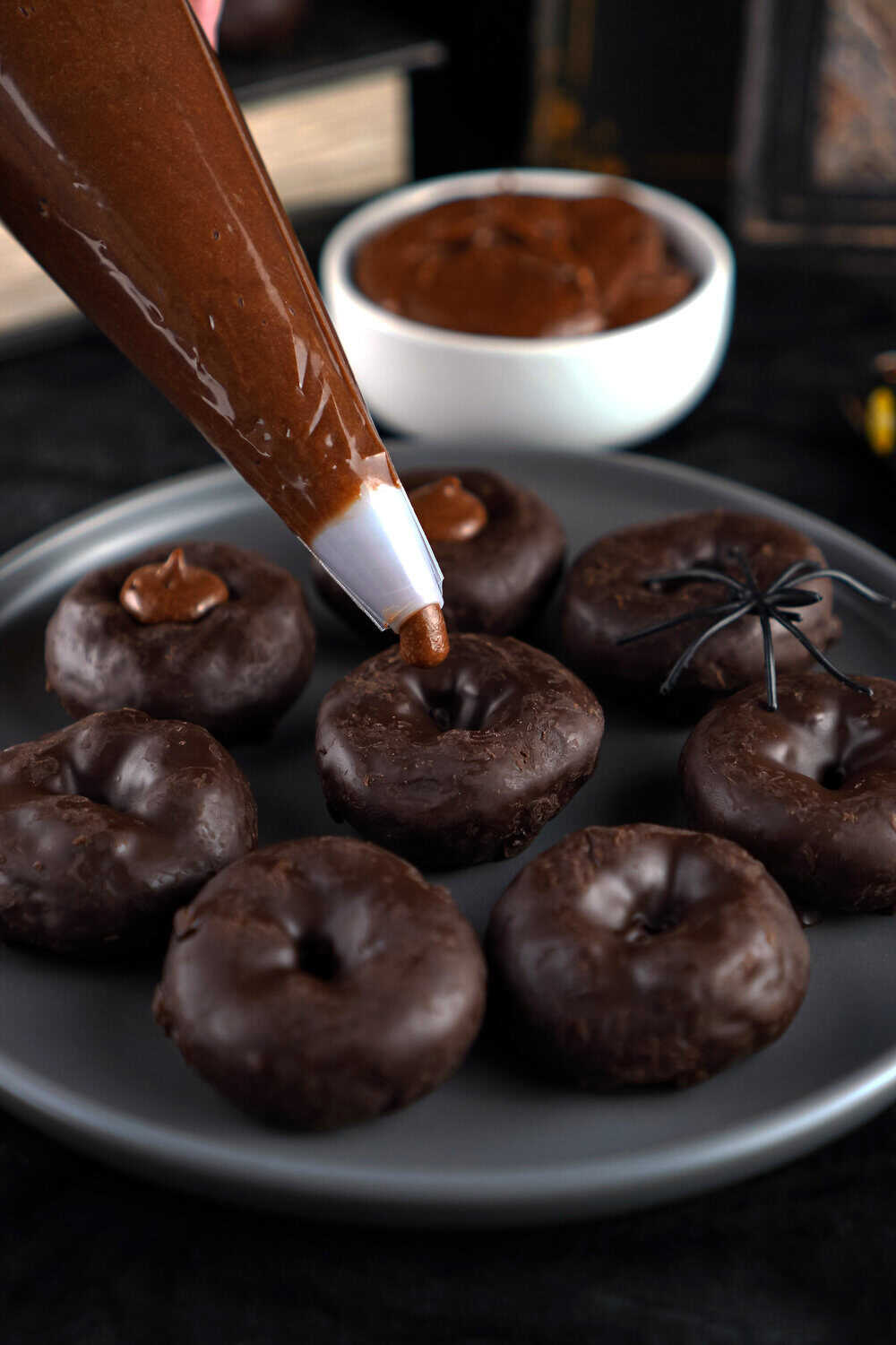 piping chocolate frosting into the center of a mini donut