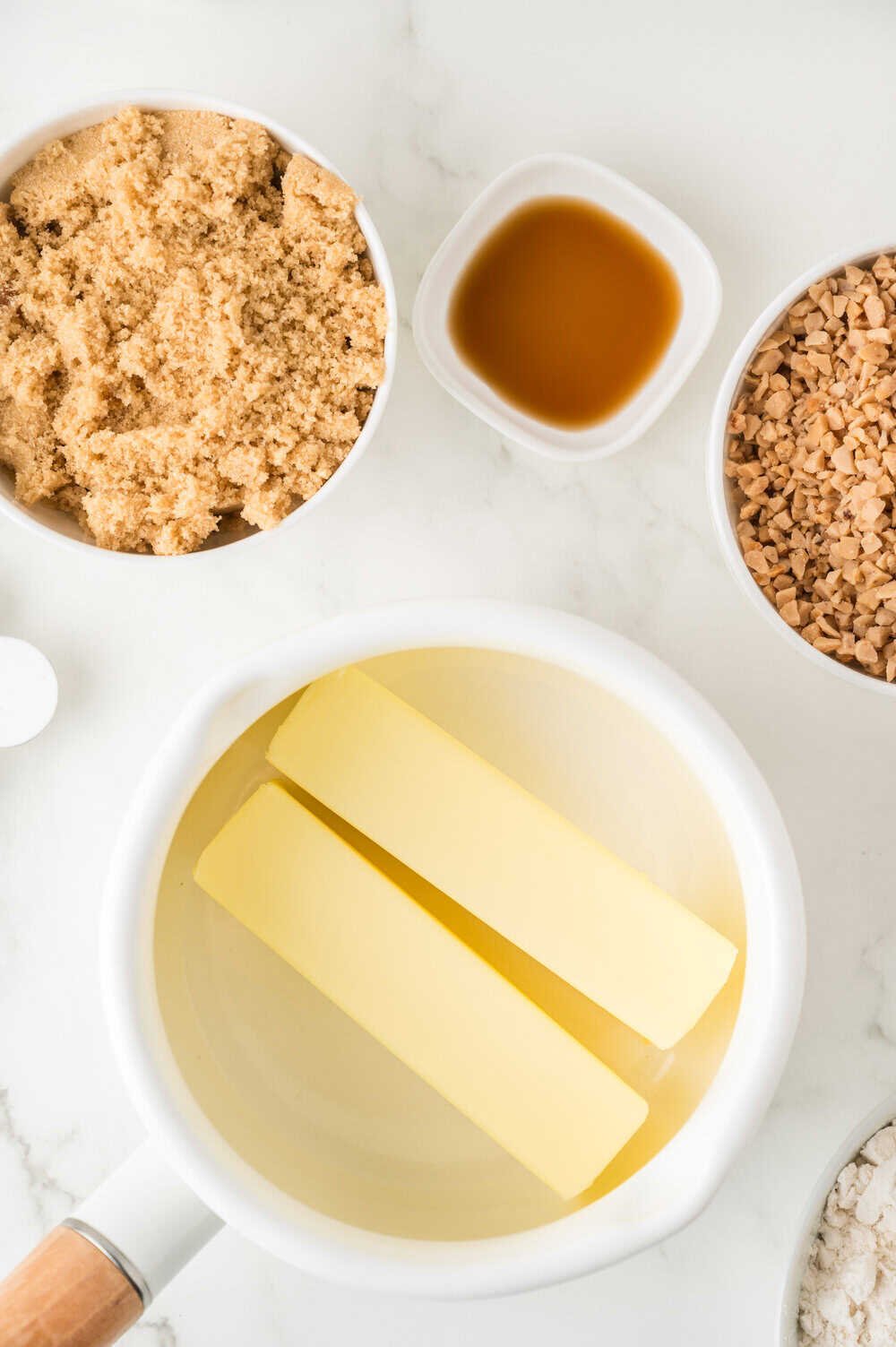 sticks of butter in a saucepan with other ingredients surrounding the pot