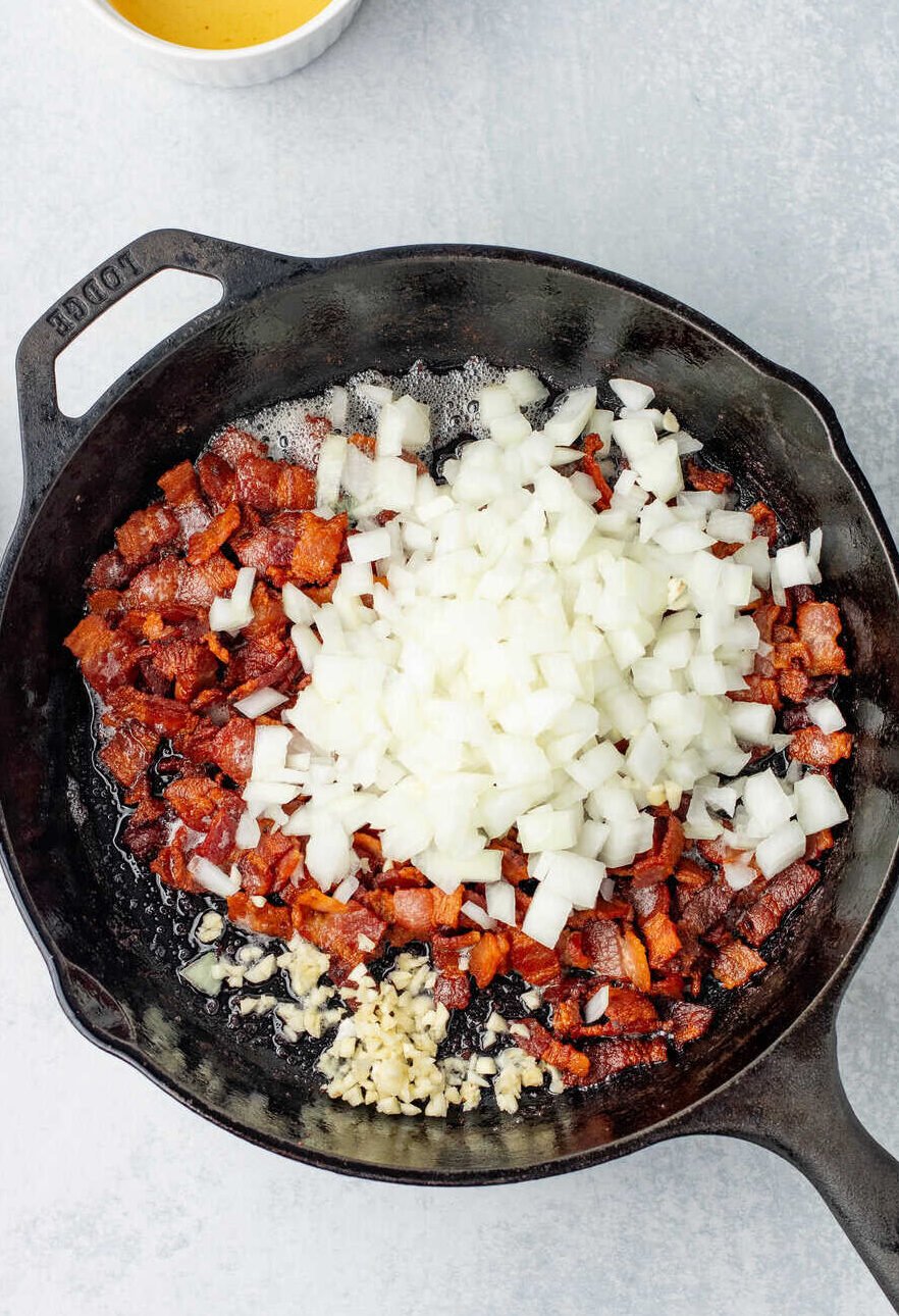 onions and garlic added to crispy fried bacon in skillet