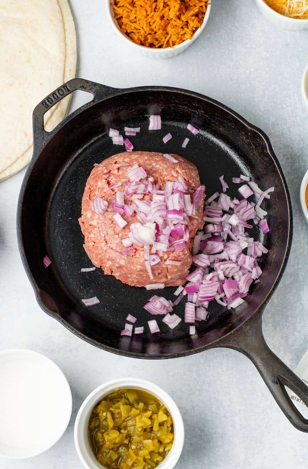 raw ground beef and diced red onion in a cast iron skillet