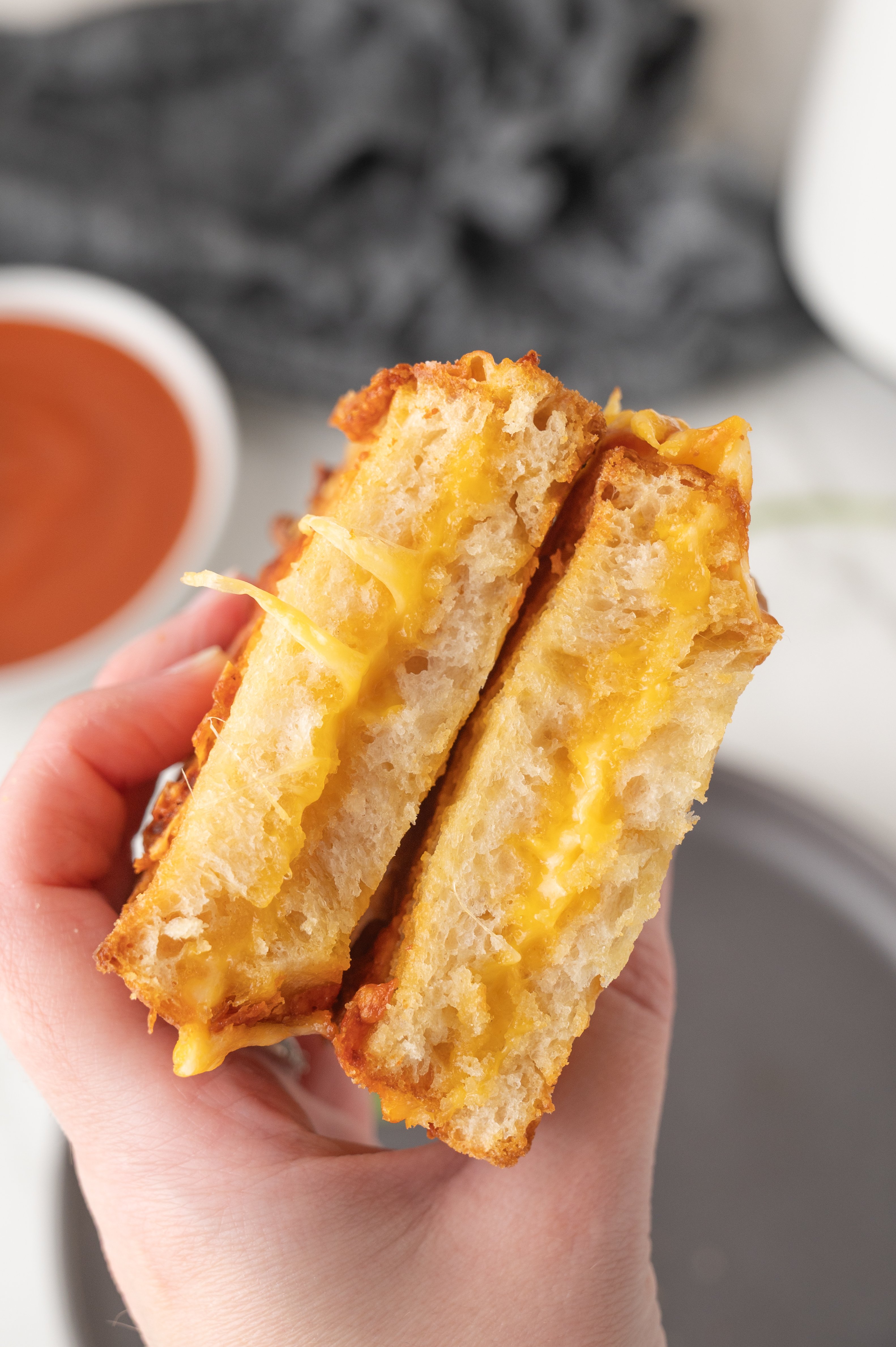 air fryer grilled cheese cut in half and being held over bowl of tomato soup