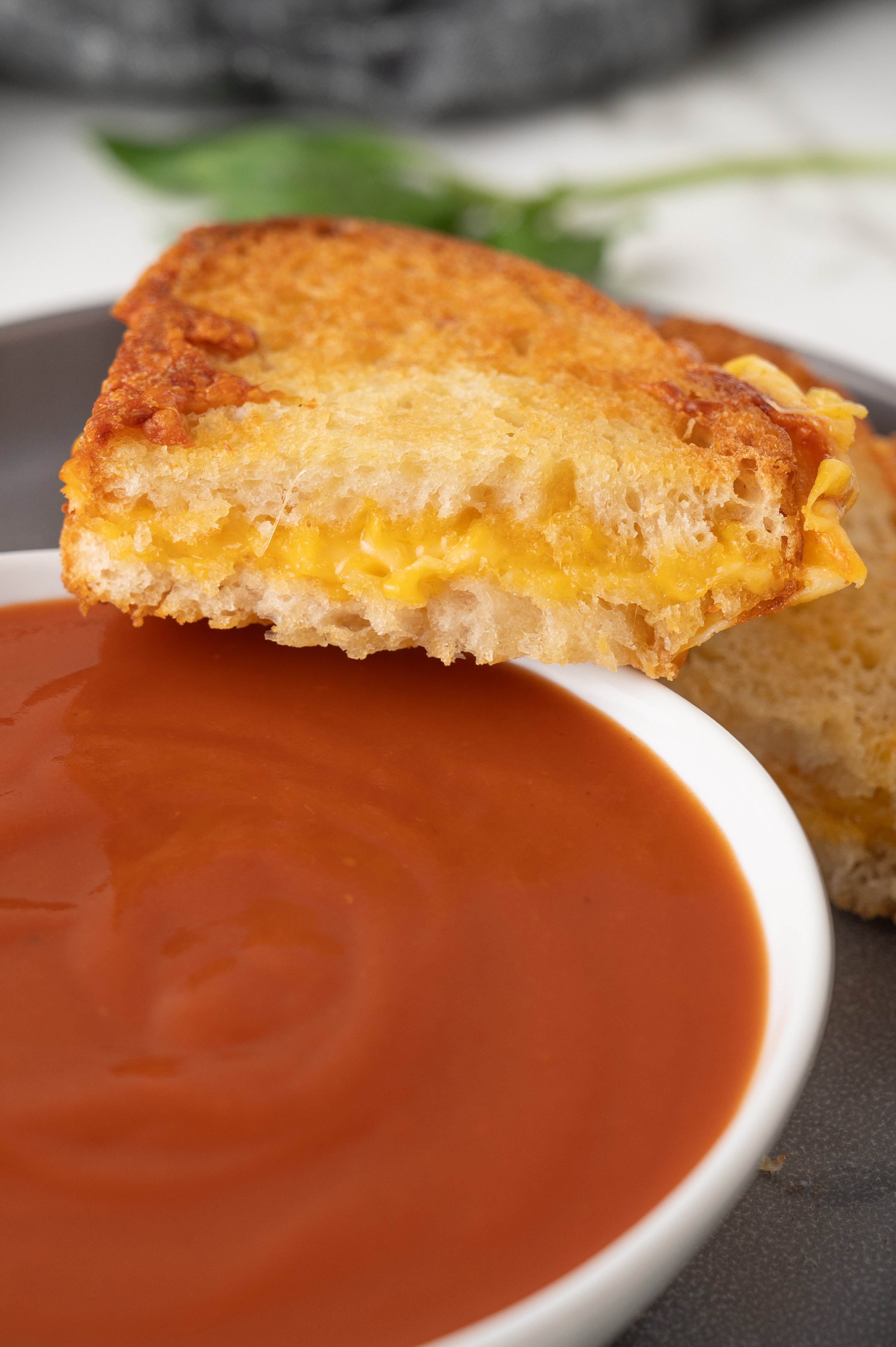 slice of grilled cheese sandwich on the side of a bowl of tomato soup