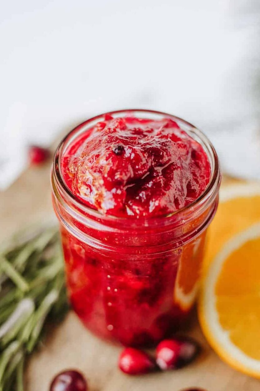cranberry jam in a mason jar on a cutting board with orange slices and fresh cranberries