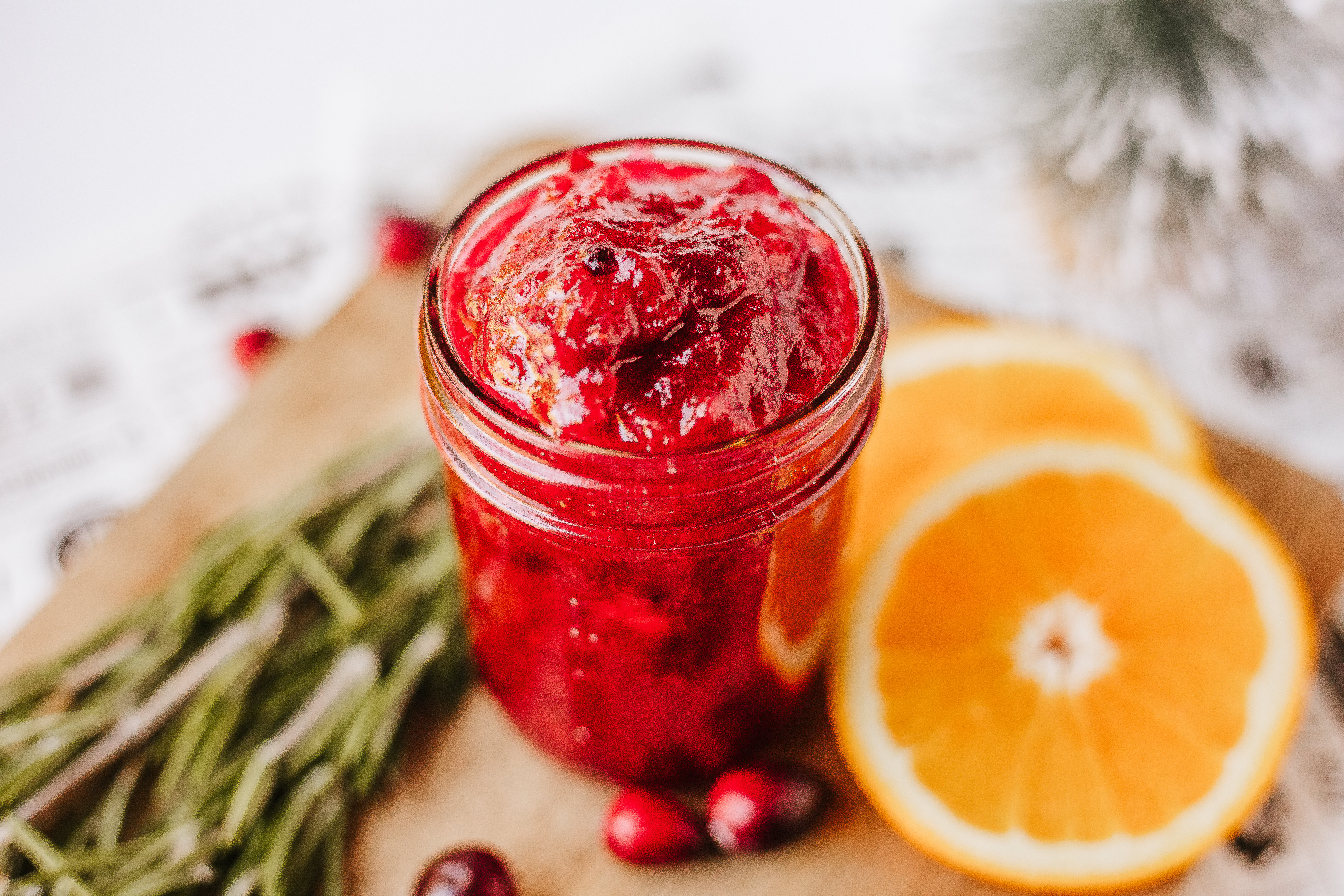cranberry jam in a mason jar on a cutting board with orange slices and fresh cranberries