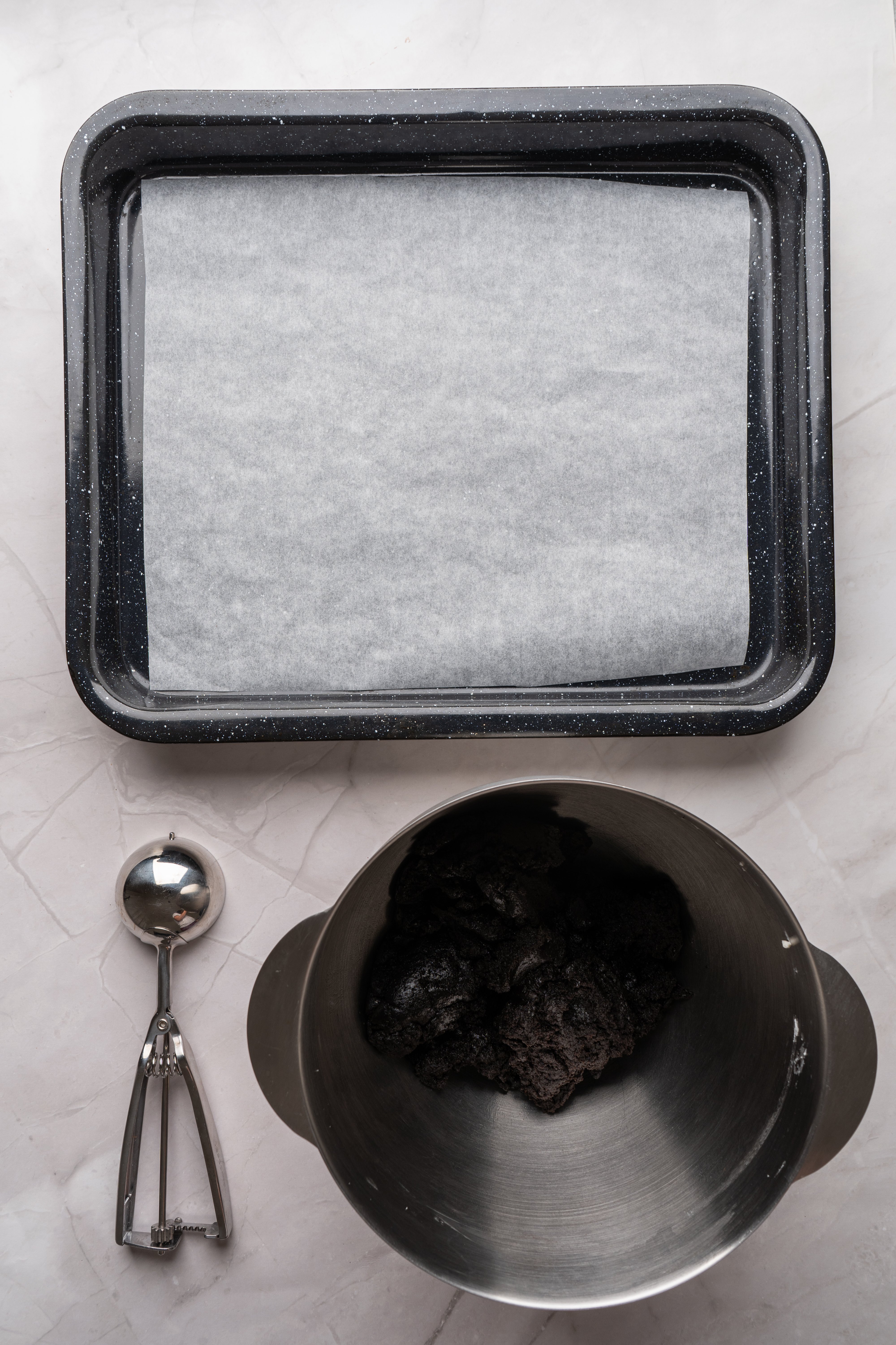 oreo balls dough in mixer bowl next to sheet with parchment paper and cookie scoop