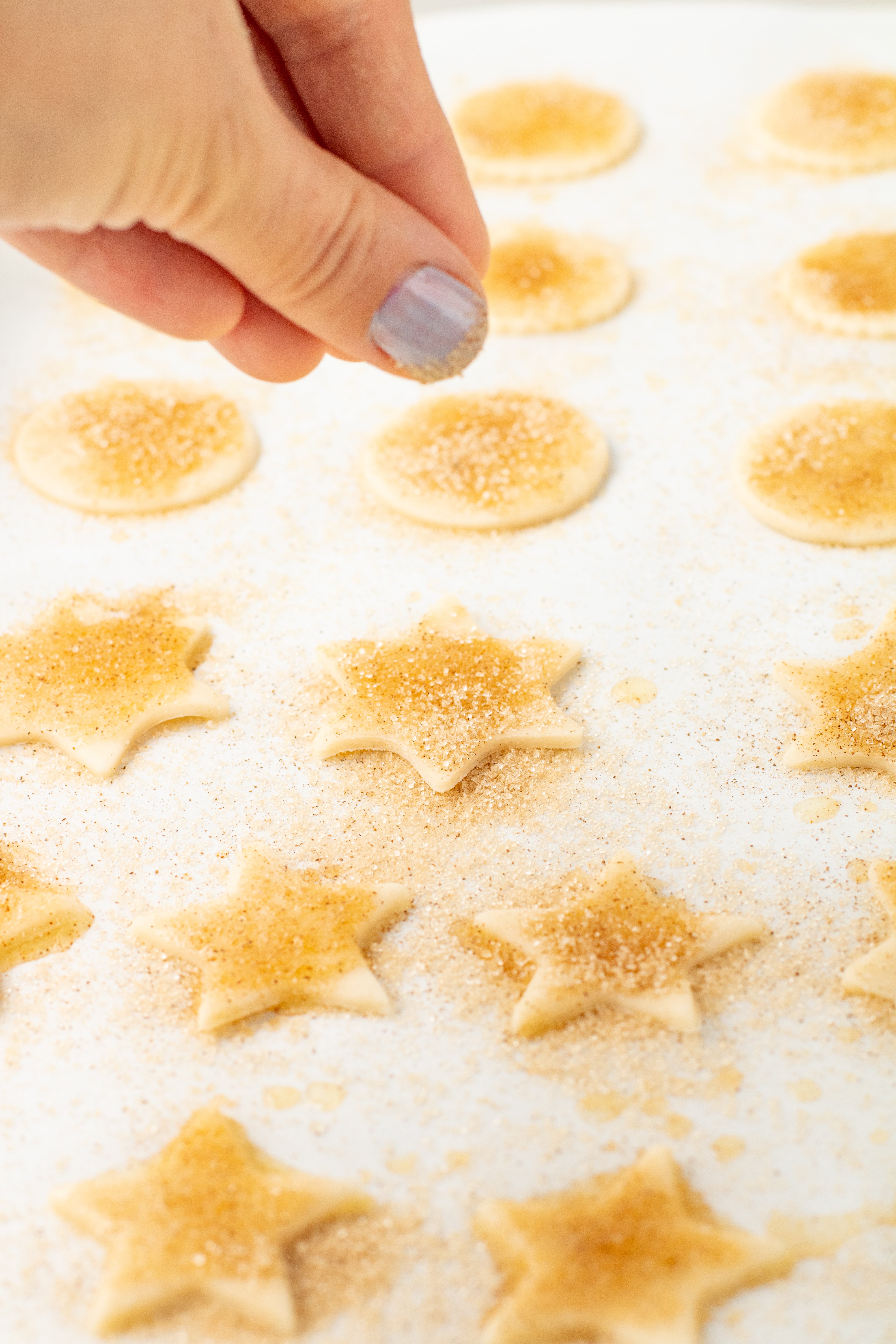 sprinkling cinnamon sugar over pie crust cookies on parchment paper